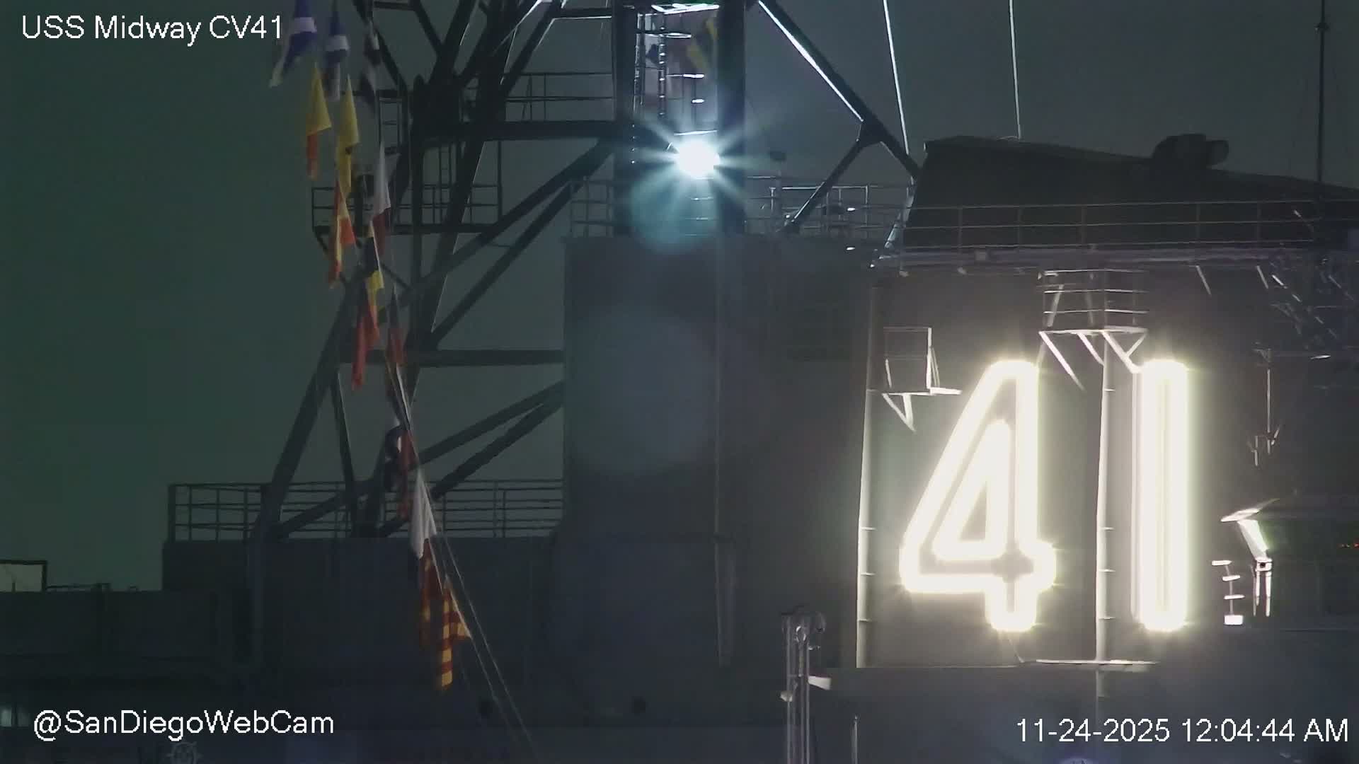 A nighttime view of a ship's structure displaying large, illuminated numbers "41" on its side, with a bright spotlight and a string of signal flags visible under clear skies.