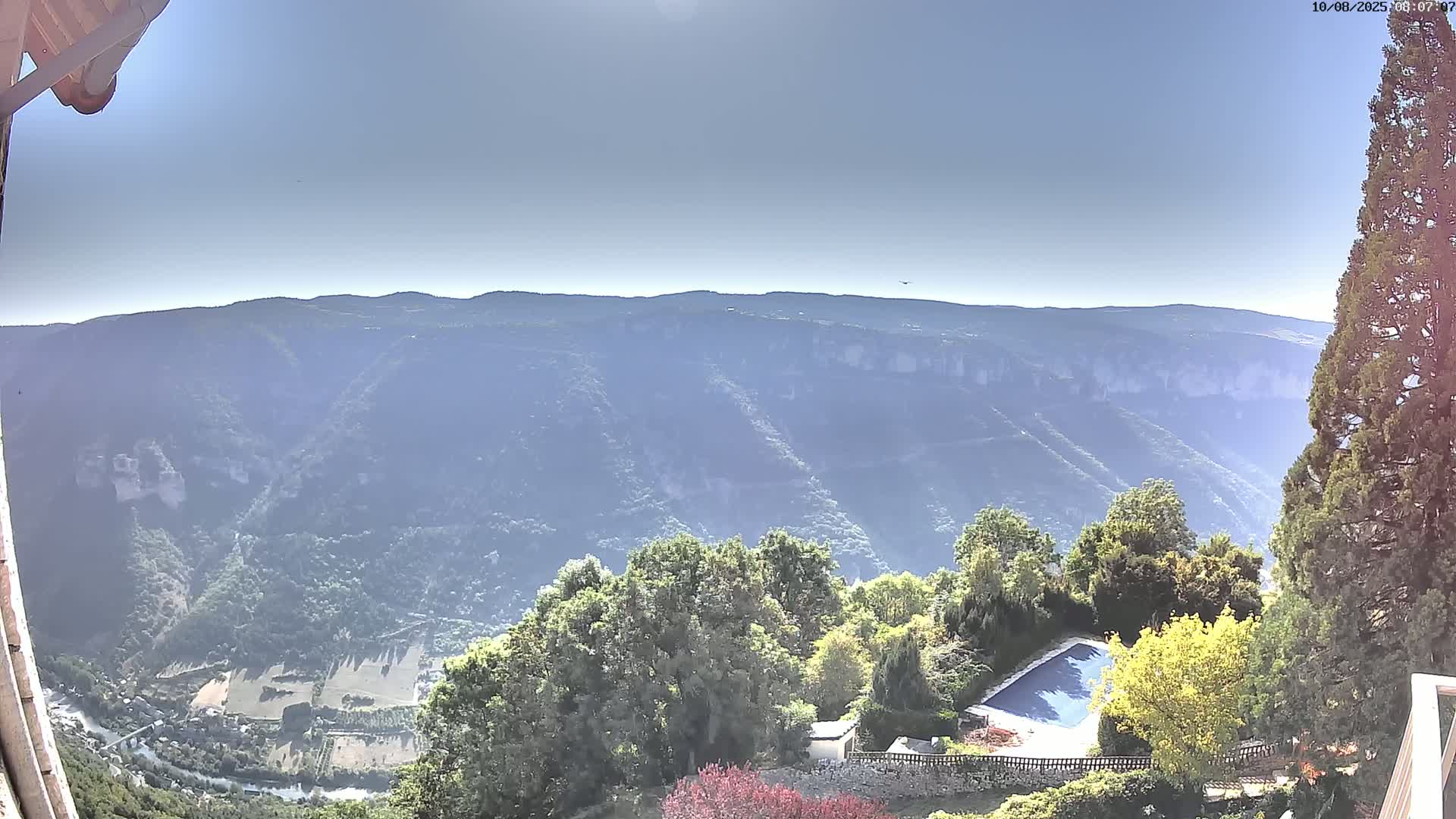 A sunny outdoor view shows a swimming pool and surrounding greenery overlooking a valley and distant mountains.