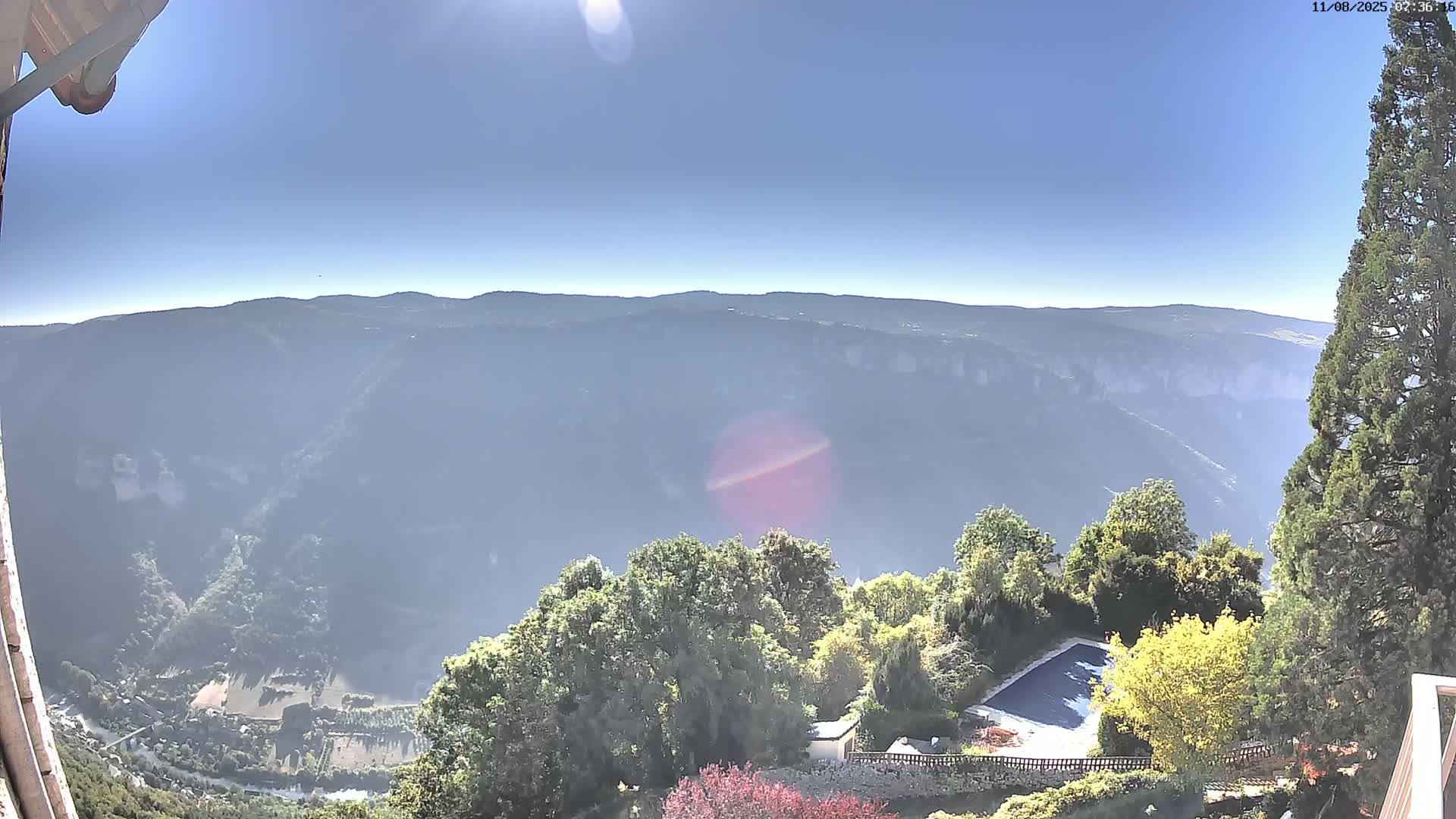 A high-angle, sunny view shows a swimming pool and trees on a property overlooking a vast, hazy valley and distant mountains.
