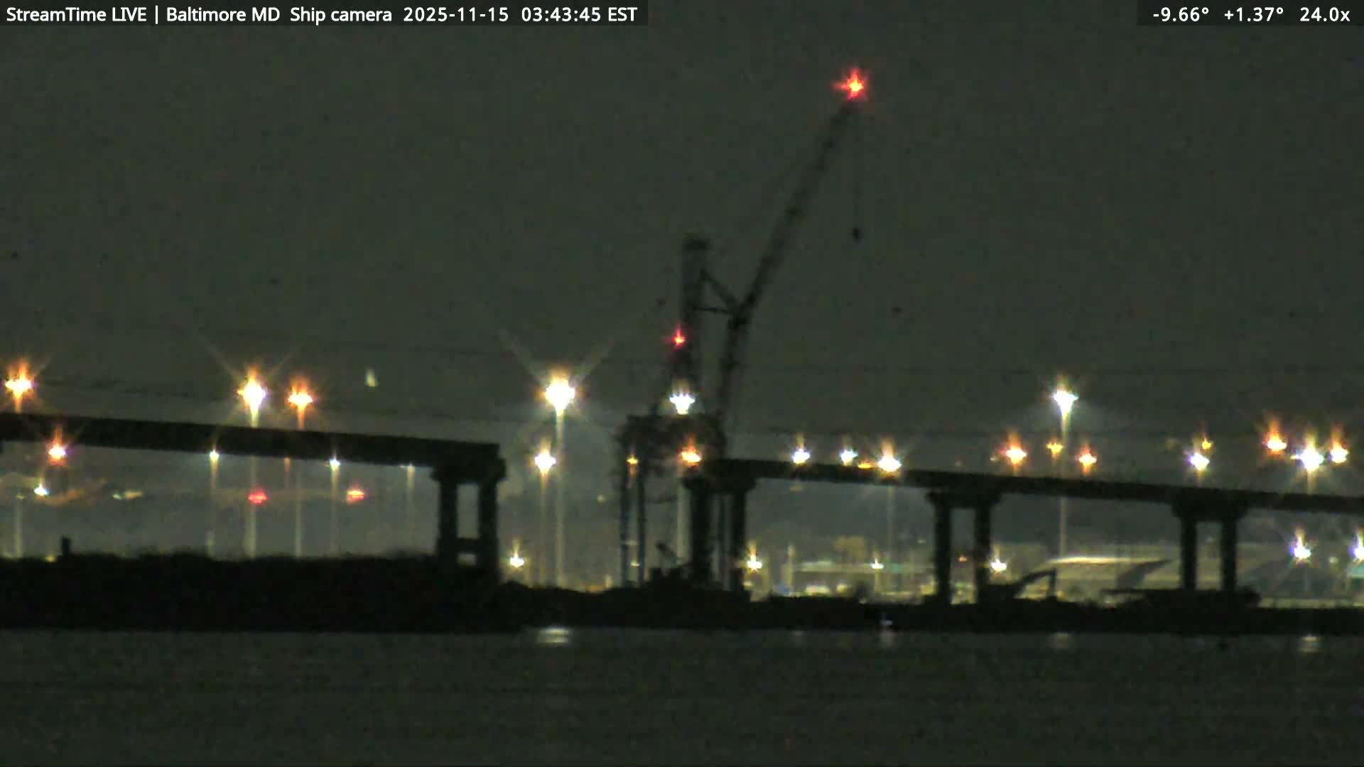 A dark and possibly foggy night scene reveals a bridge illuminated by numerous starburst streetlights over a body of water, with an industrial crane visible in the background.