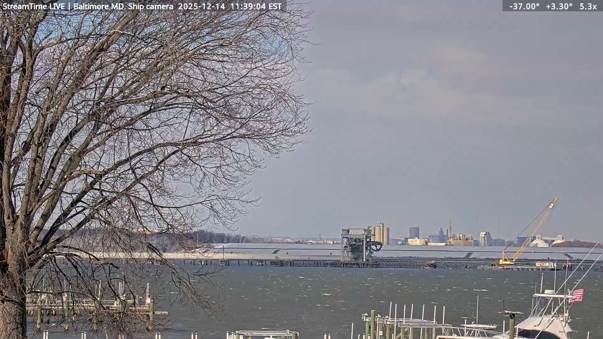 A clear night view shows a dark waterfront with reflections of numerous bright city or industrial lights across the horizon, punctuated by several red beacons in the sky.