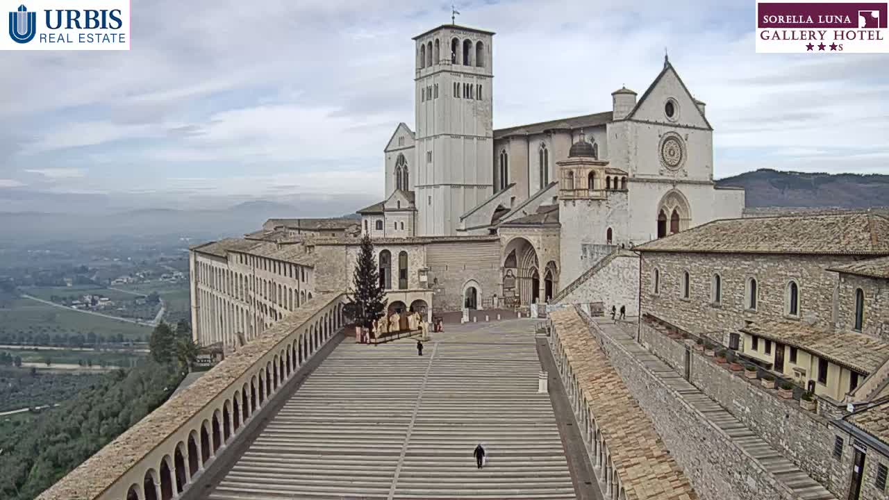 A large, light-colored basilica complex sits atop a hill overlooking a valley on an overcast day.