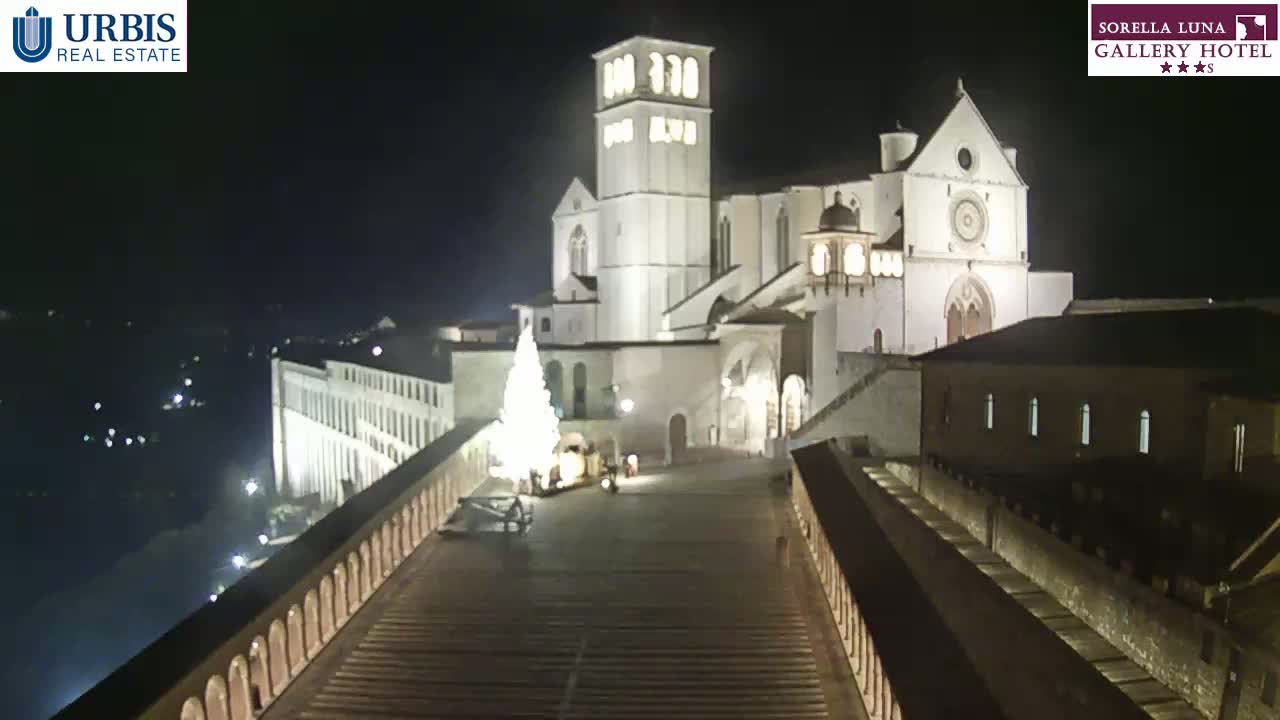 A large, illuminated building complex, possibly a church, is visible at night, with a decorated Christmas tree in the foreground and a long staircase leading to it.