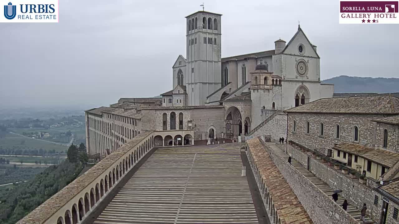 A large stone basilica complex sits atop a hill on an overcast day, overlooking a valley.