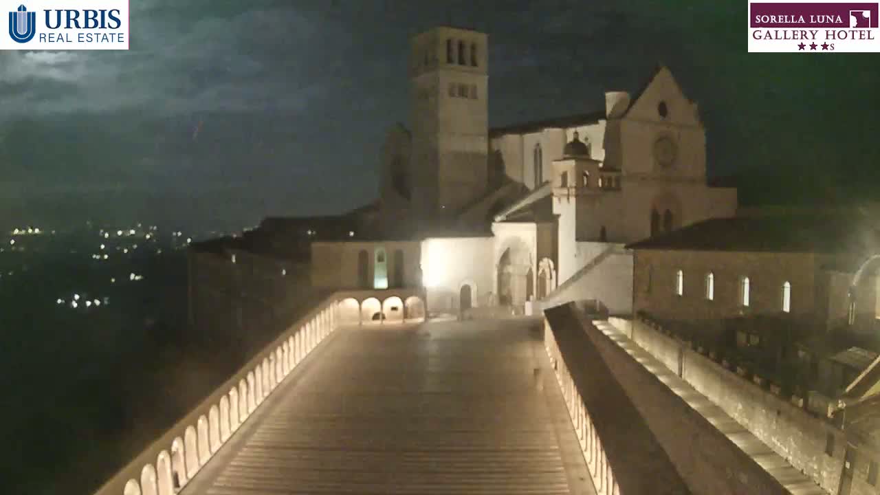 A nighttime view of a large stone building, possibly a church or monastery, illuminated against a partly cloudy sky.