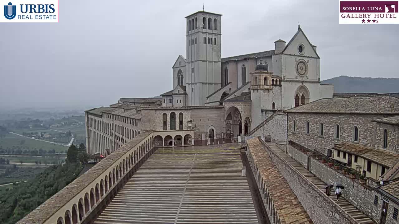 A large stone basilica and attached buildings overlook a long, paved walkway on a cloudy day.