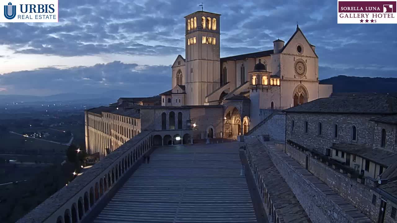 A large, illuminated basilica sits atop a hill at twilight, overlooking a valley below.