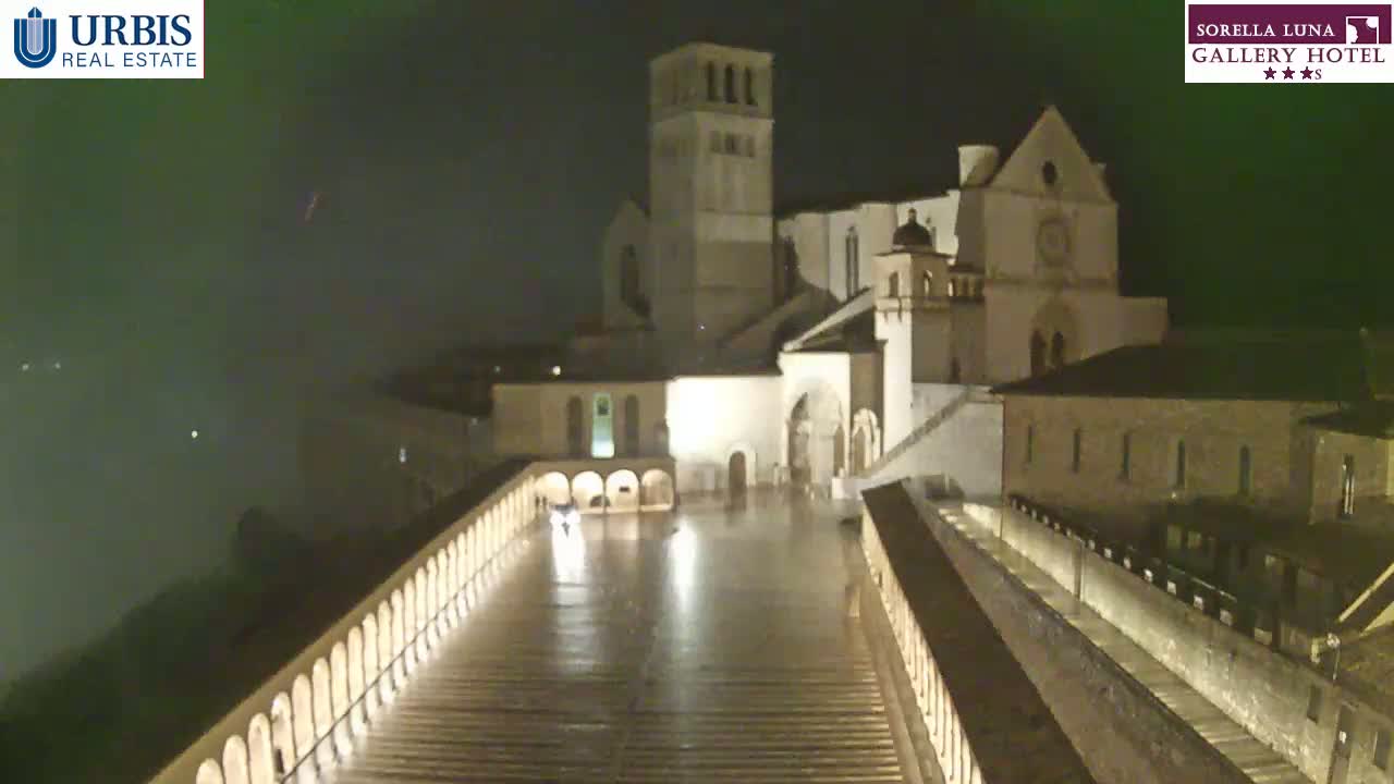 A large, illuminated stone building complex is seen at night in rainy conditions.