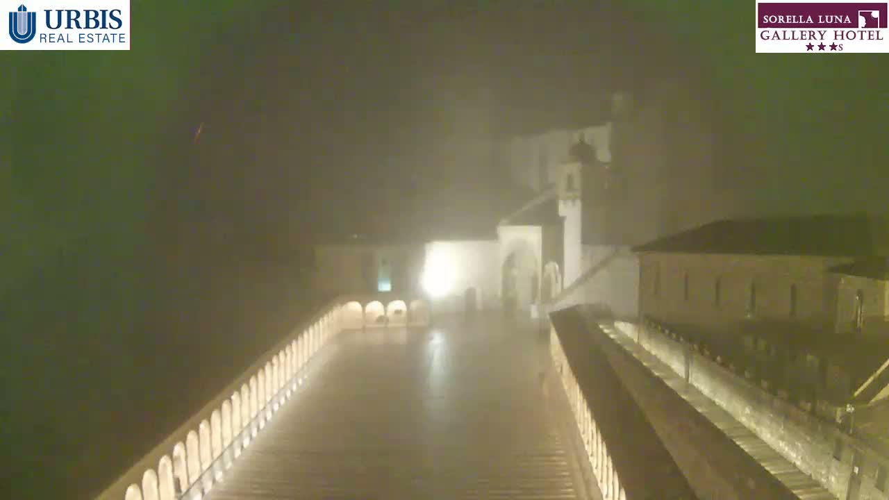 A nighttime view of a courtyard, enclosed by buildings, is obscured by heavy fog or mist.