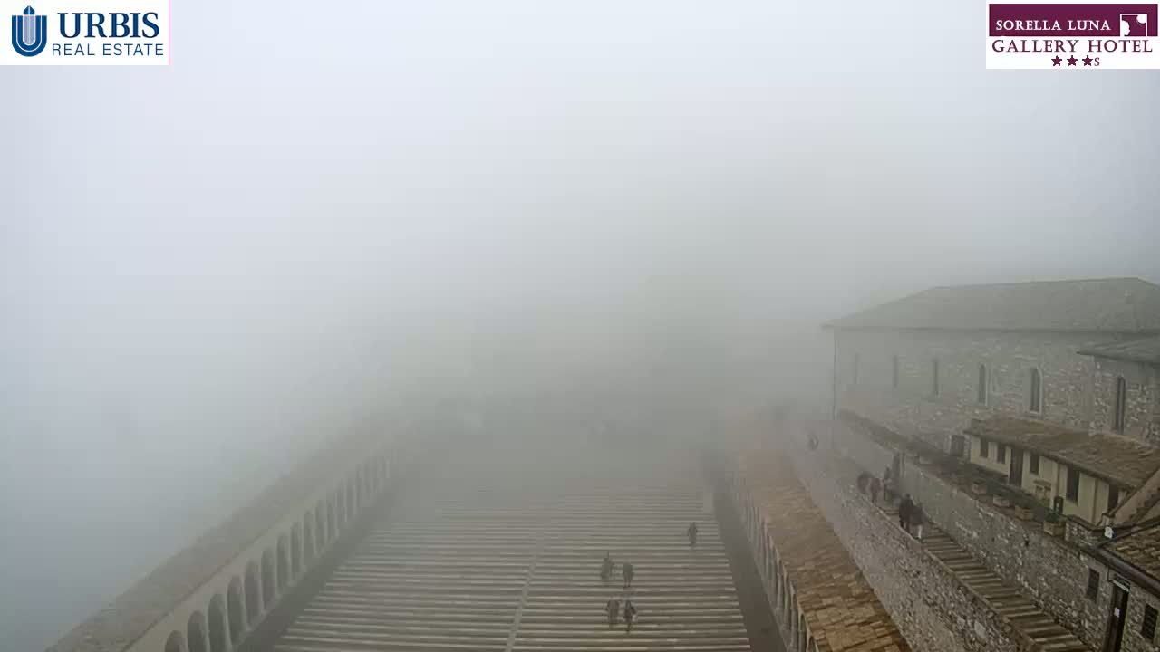 A stone building and long staircase are barely visible through heavy fog.