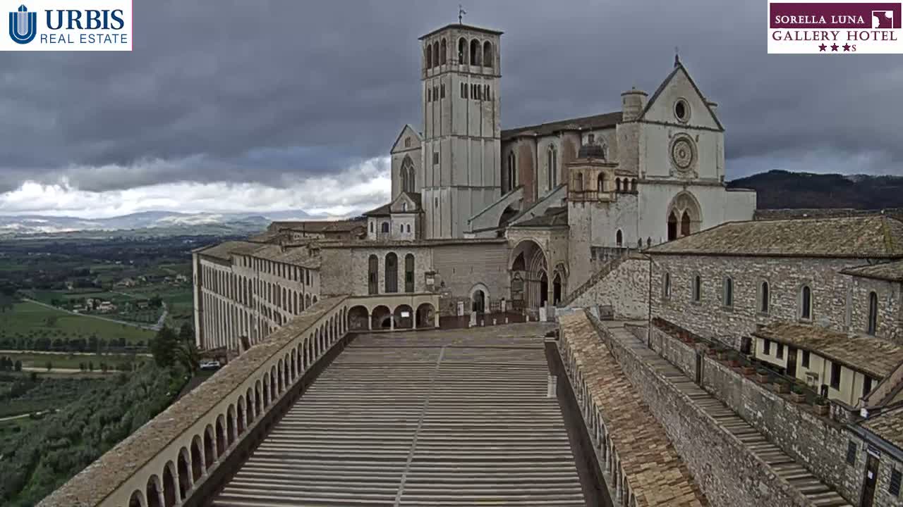 A large stone basilica and adjoining structures are viewed from above on an overcast day, overlooking a sprawling landscape.