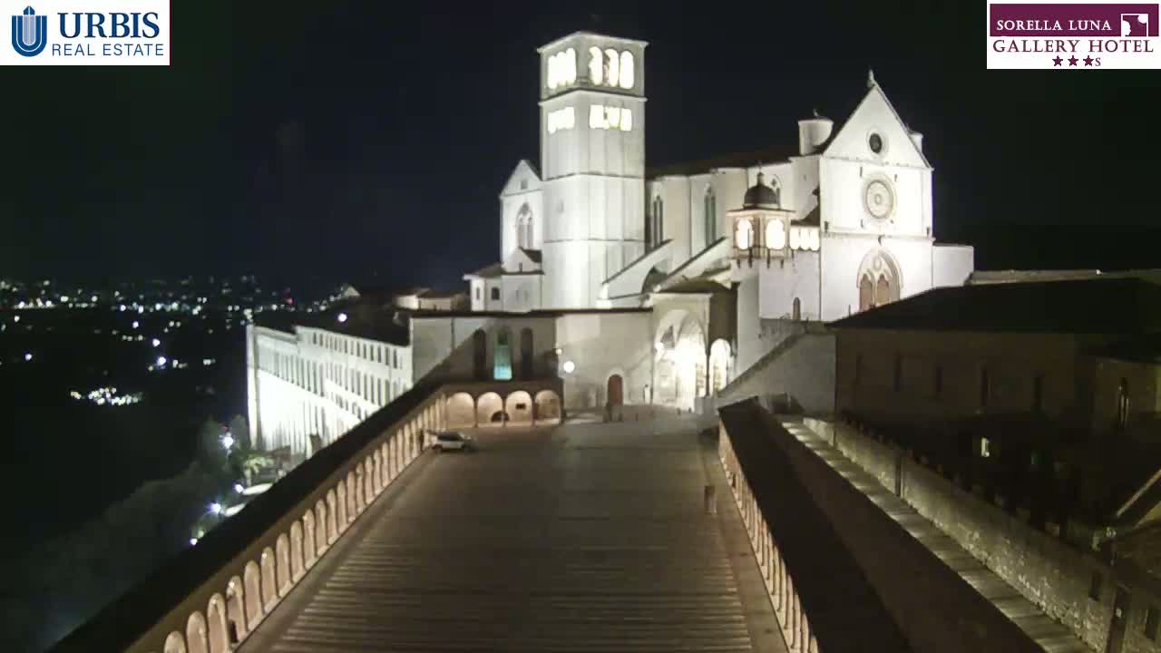 A large, illuminated basilica stands at night overlooking a city with a long paved pathway leading to it.