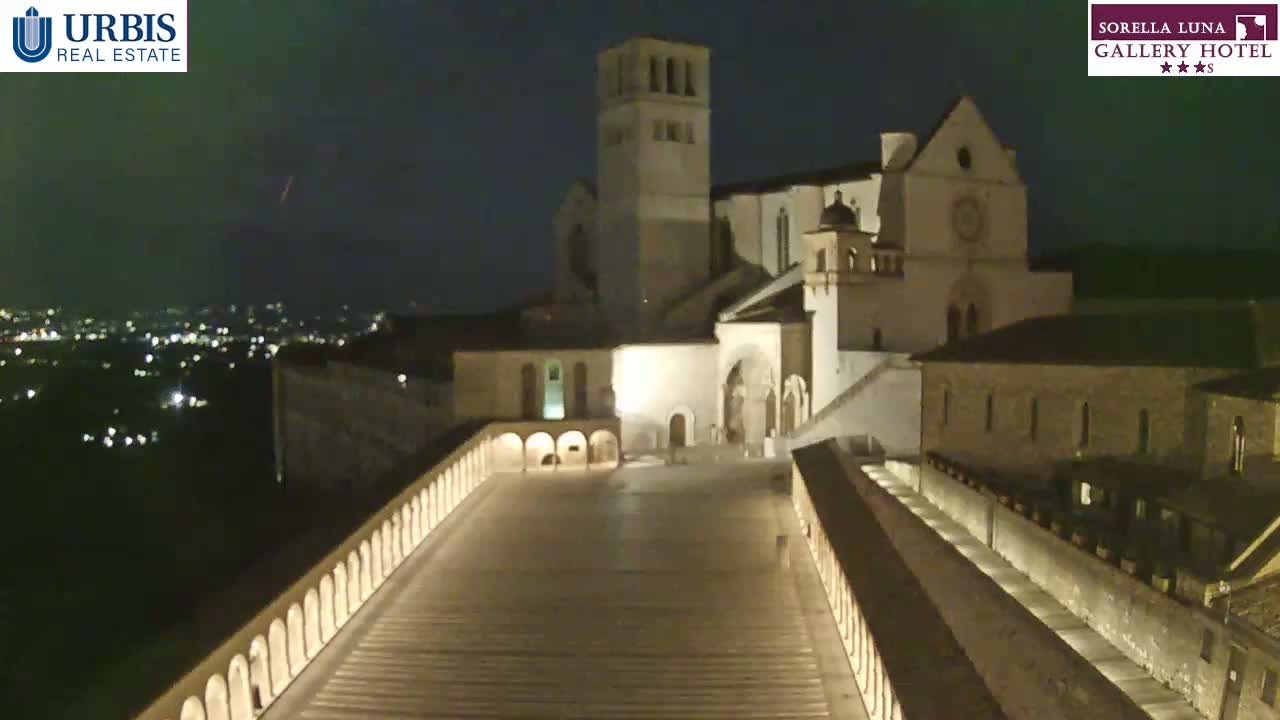 A large, illuminated basilica stands at night overlooking a city, under a mostly clear sky.