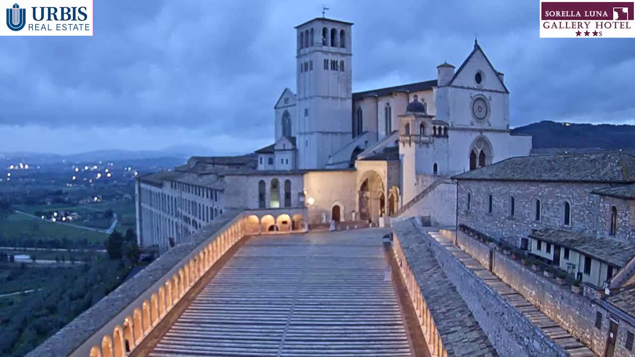 A large stone basilica is illuminated at dusk, overlooking a long, wide staircase leading to it from below.