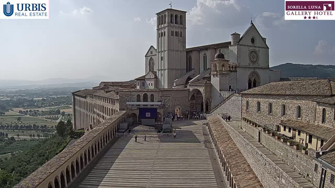 A large stone basilica complex sits atop a hill on a partly sunny day, overlooking a sprawling valley.