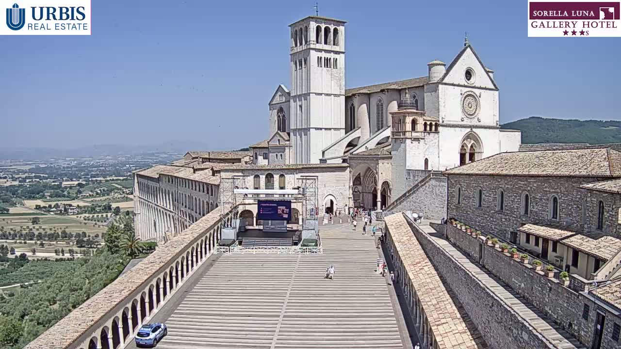 A large, light-colored basilica sits atop a hill overlooking a sprawling landscape under a clear, sunny sky.