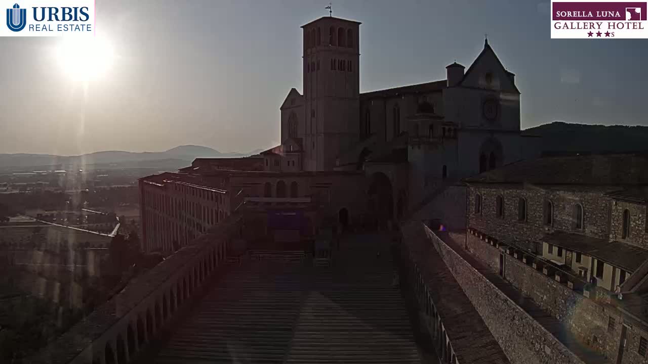 A large stone basilica sits on a hilltop overlooking a hazy valley at sunrise.