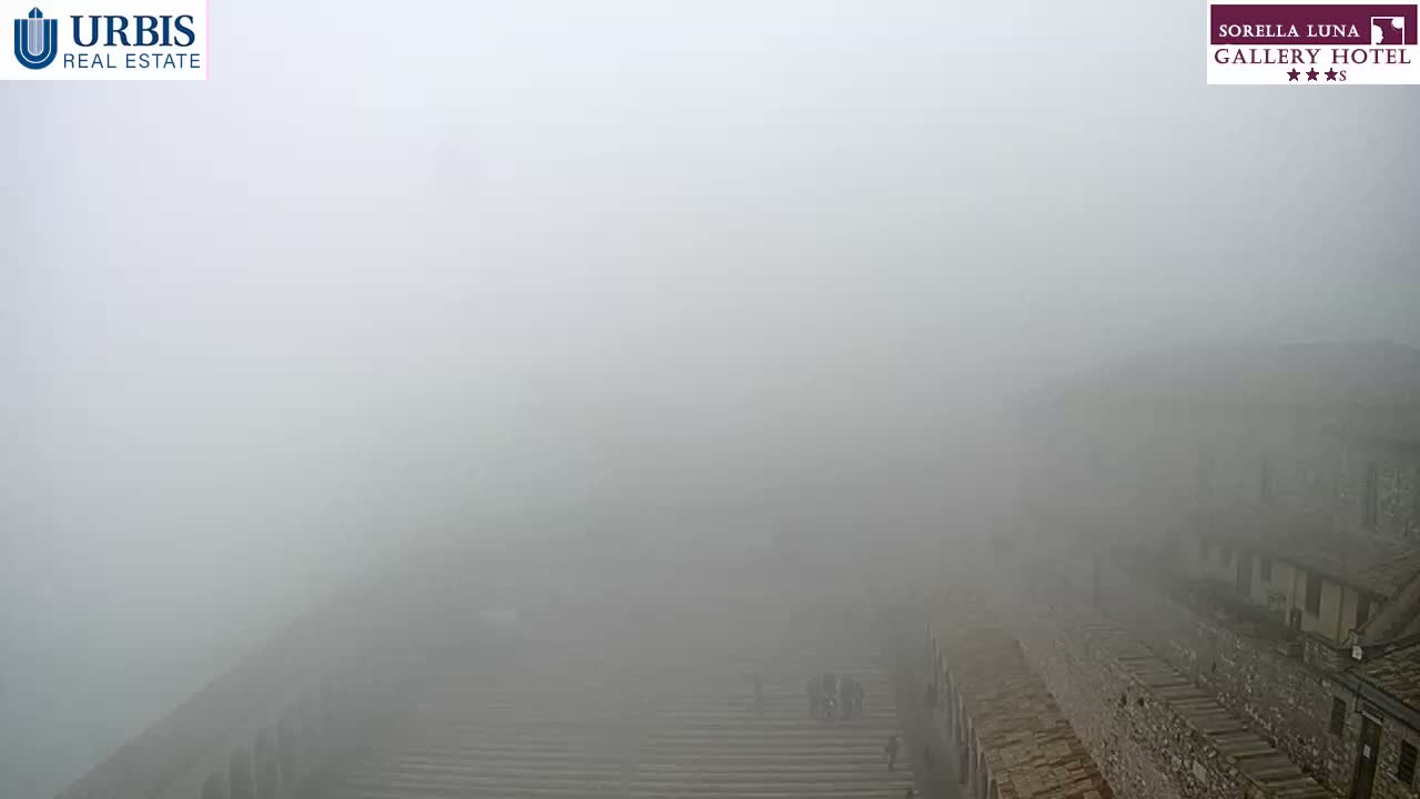 A wide outdoor view shows a large set of stone steps and traditional stone buildings partially obscured by thick fog, with several people visible on the steps.