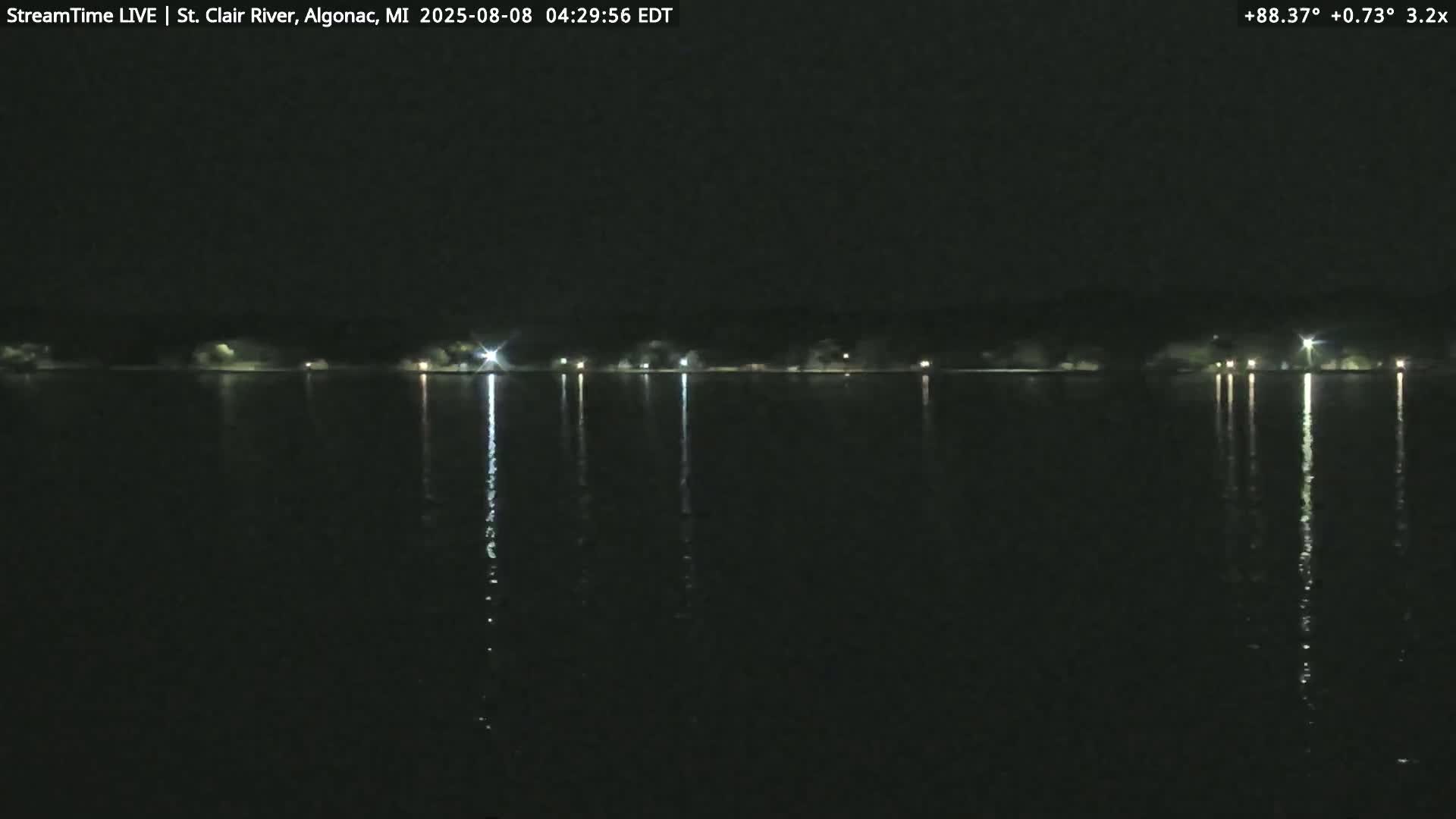 At night, the lights of a distant shoreline are reflected in a calm, dark body of water.