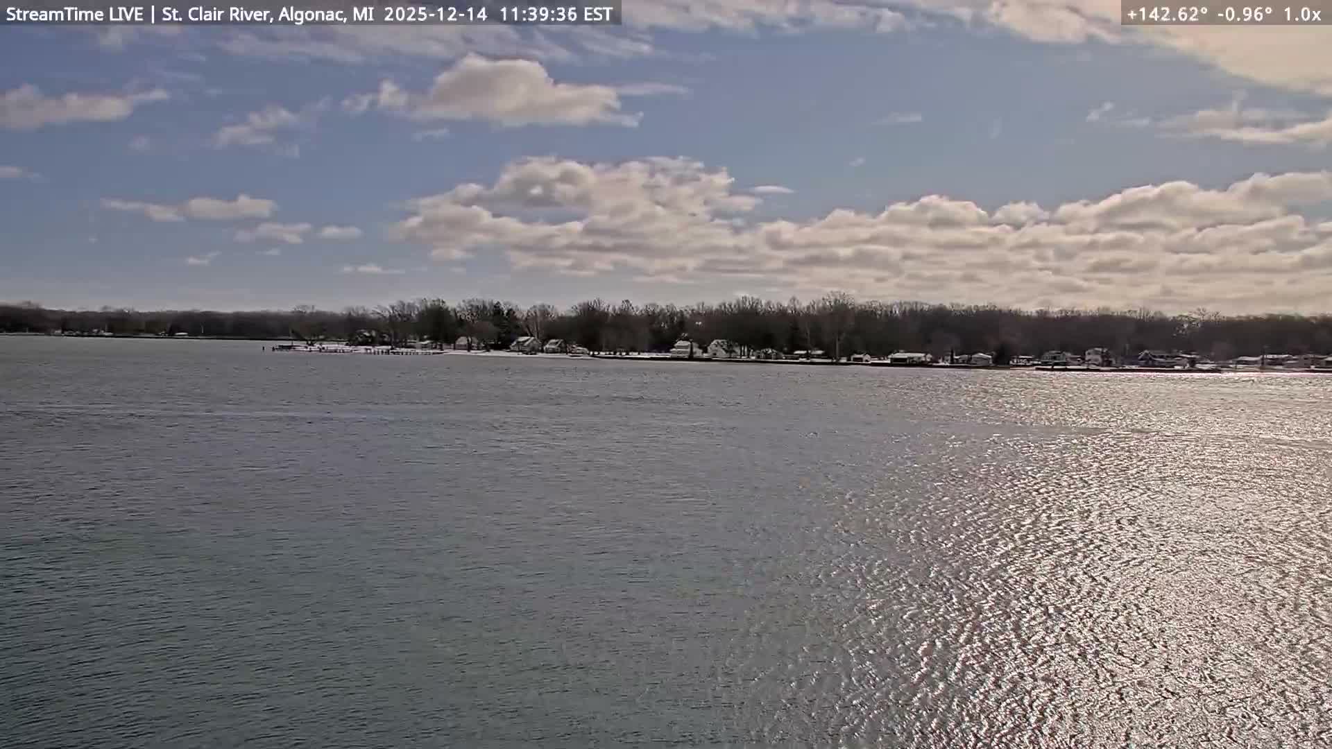 A dark nighttime view shows a body of water in the foreground with a line of distant lights visible across the opposite shore under clear conditions.