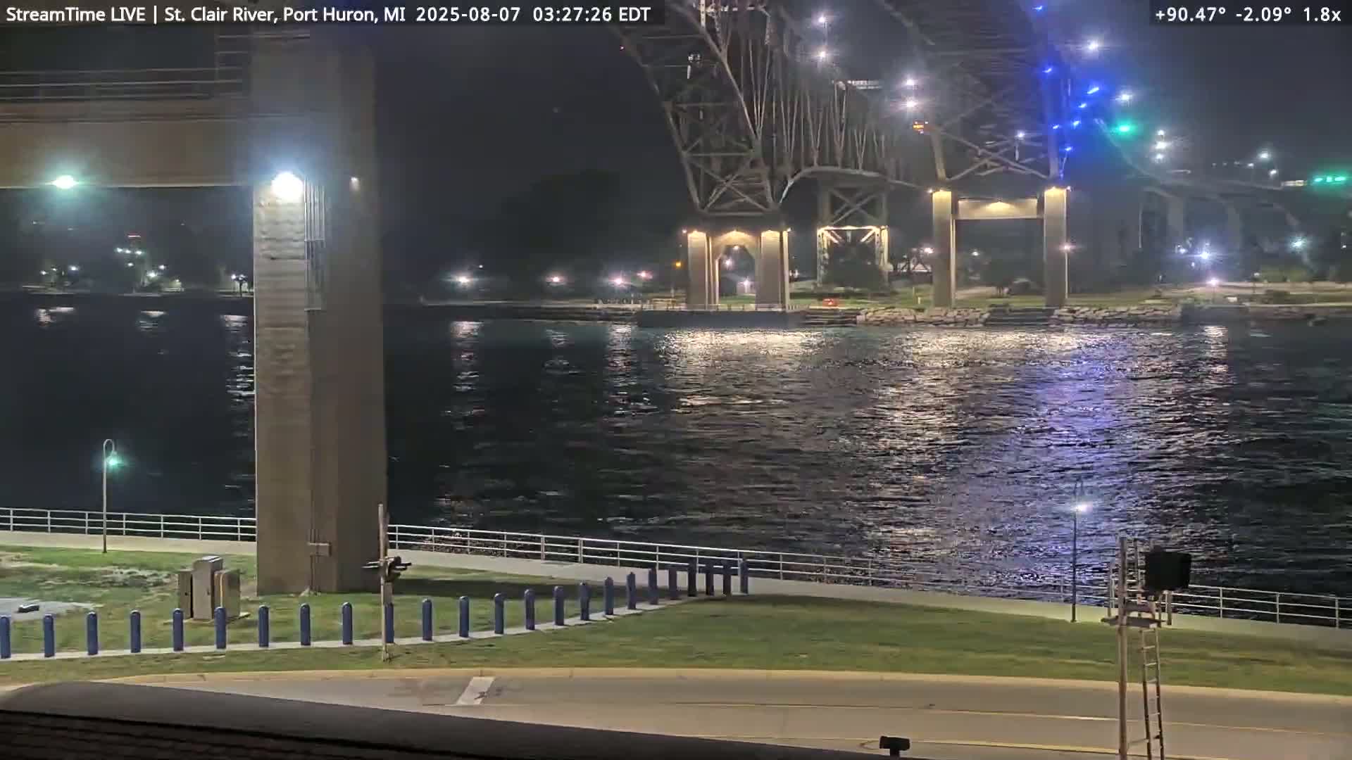A nighttime view of a river with a large illuminated bridge in the background under a clear sky.