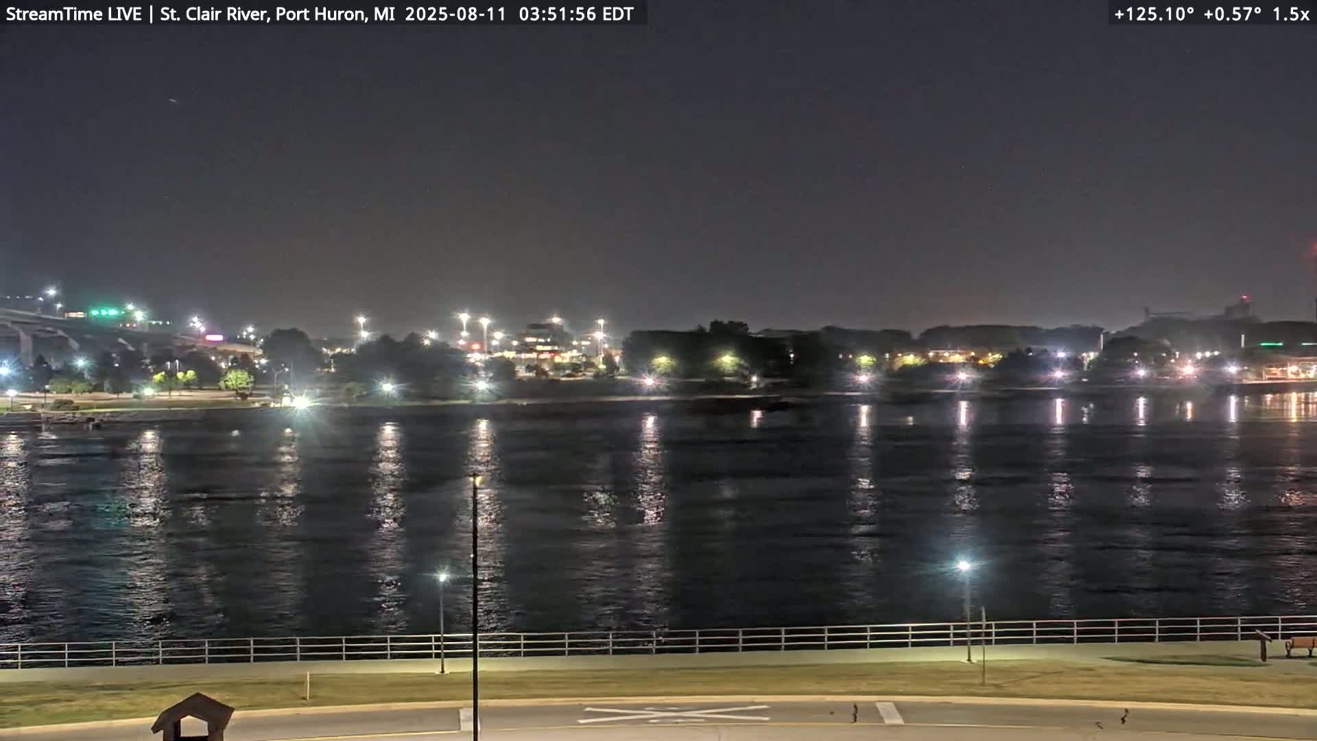 A nighttime view of a calm river reflecting city lights under a clear, dark sky.