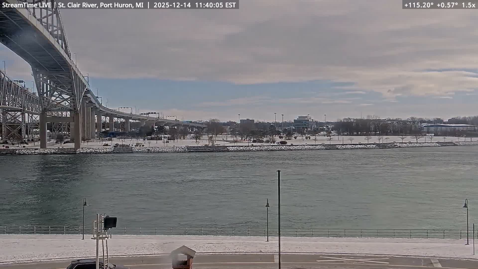 A wide river flows at night, reflecting numerous city lights from both banks and a brightly illuminated bridge on the left, under an overcast sky.