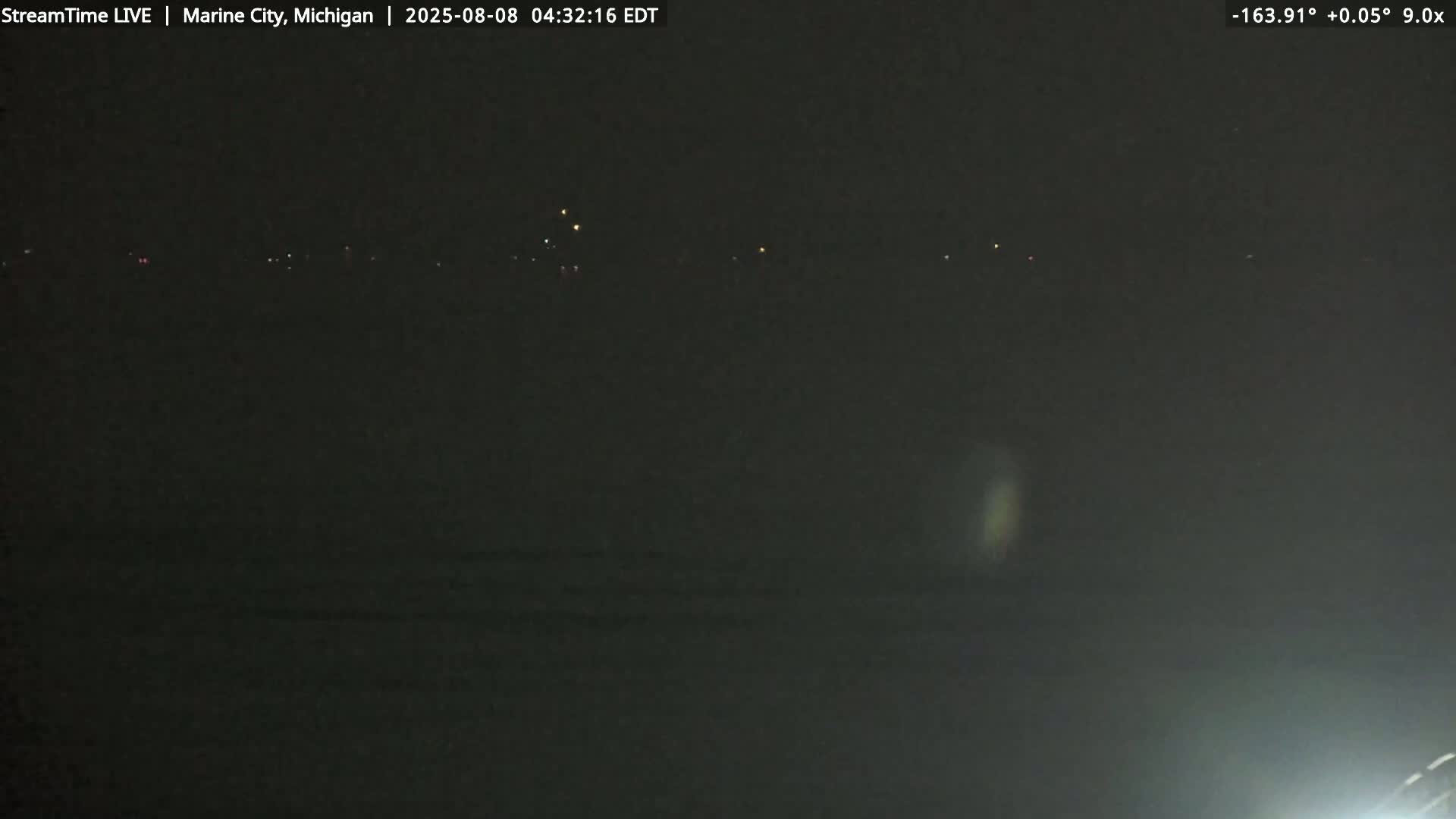 A dark nighttime scene shows a body of water with a distant line of lights on the horizon.