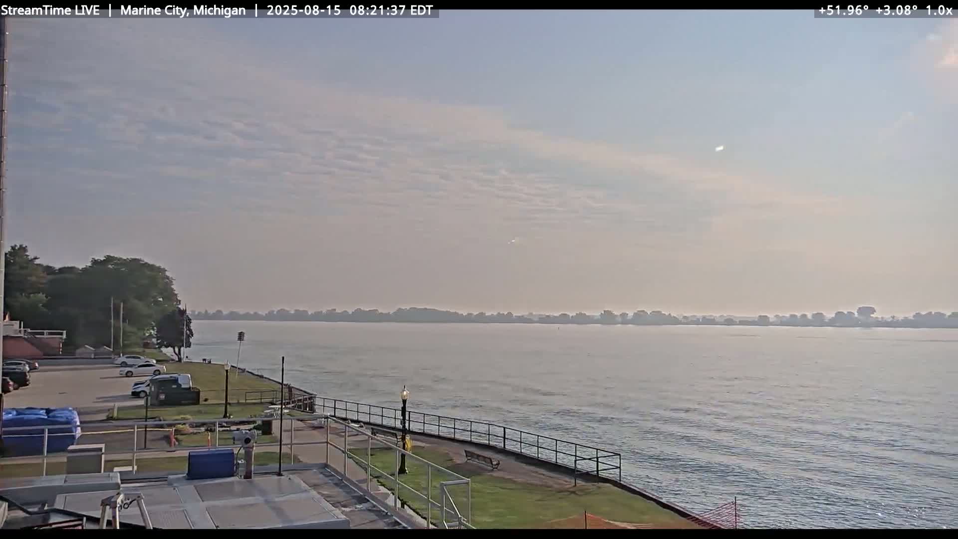 A calm body of water stretches out to a tree-lined shoreline under a partly cloudy sky.