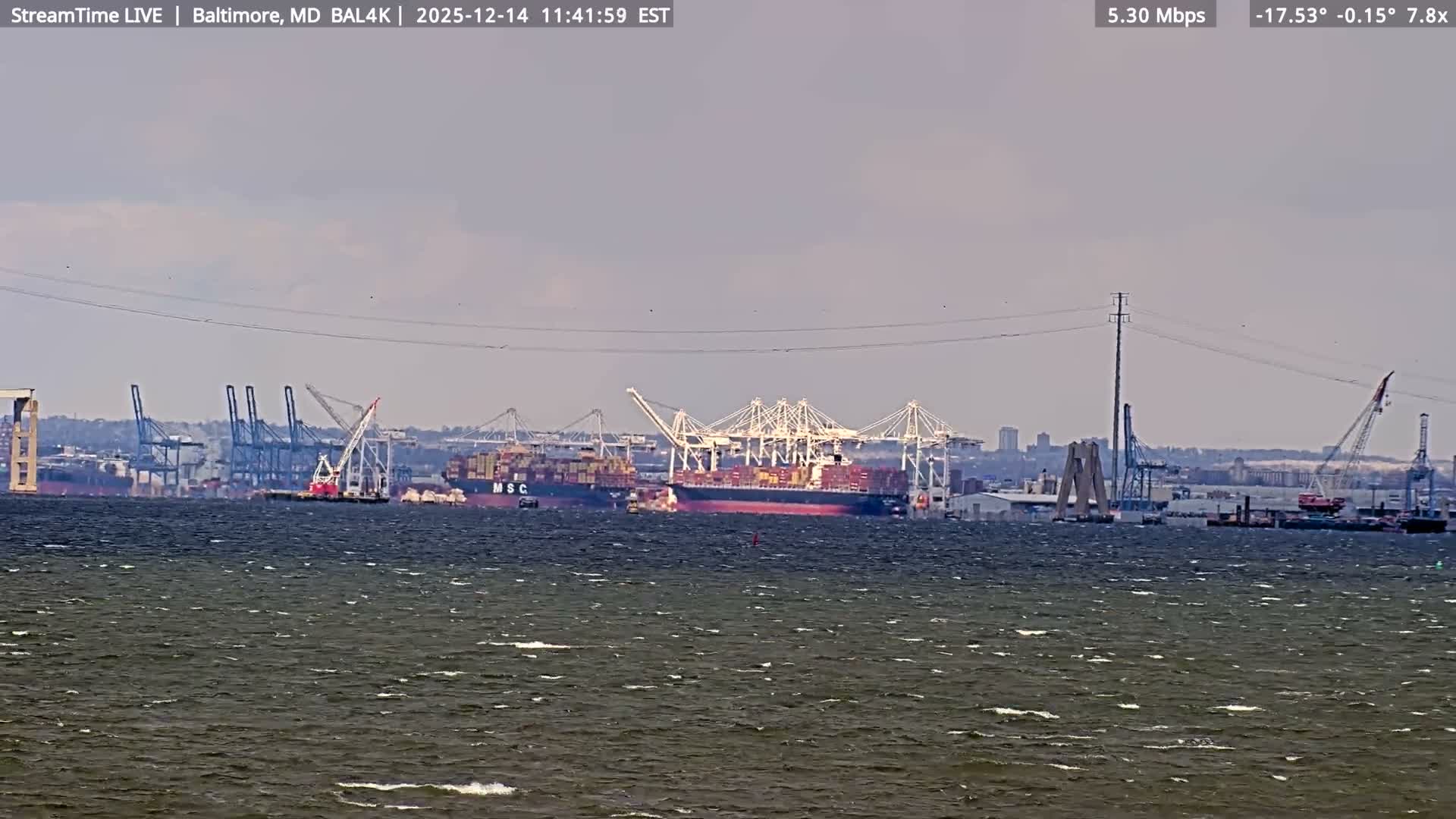A vast expanse of calm dark water reflects the numerous brightly lit cranes and industrial structures of a busy port under a clear night sky.