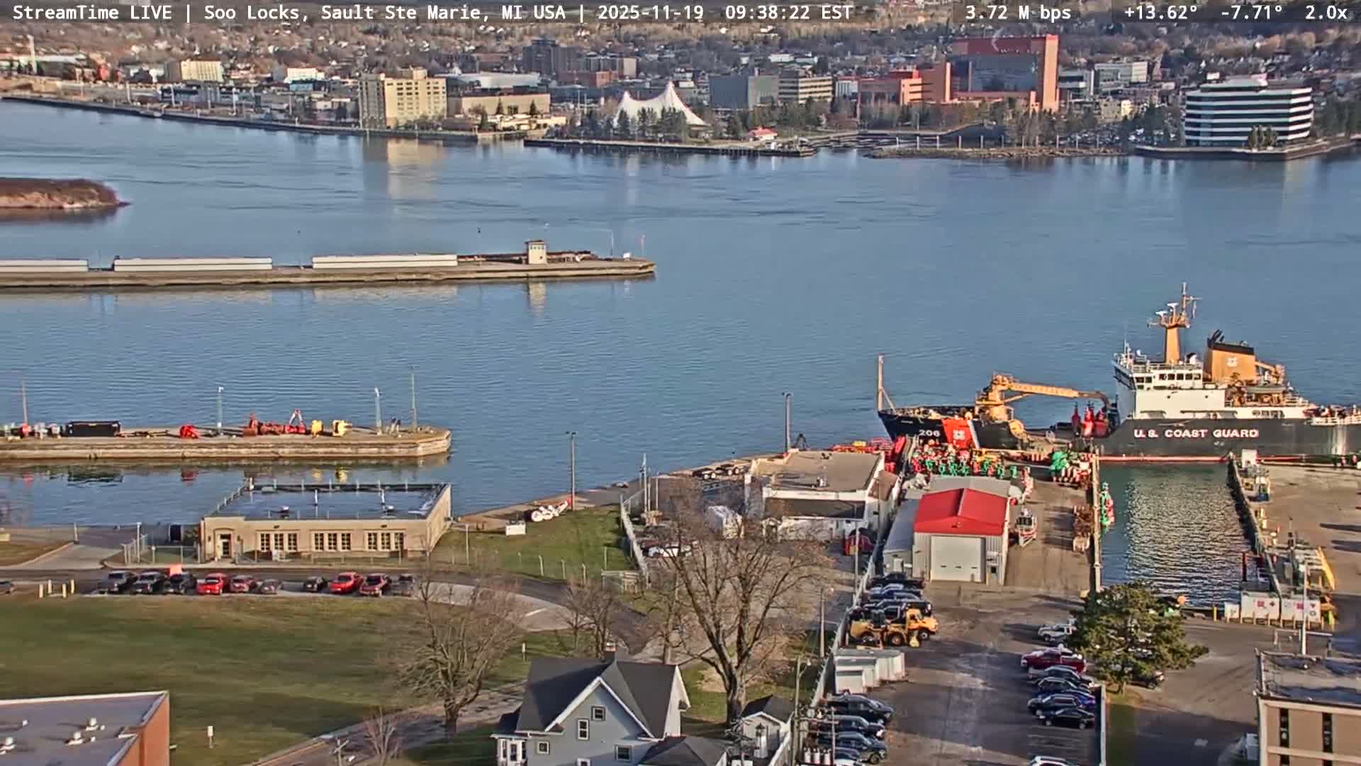 The image shows a clear, dark night view of a waterfront area with numerous lights illuminating buildings, docks with boats, and reflecting across the still water.