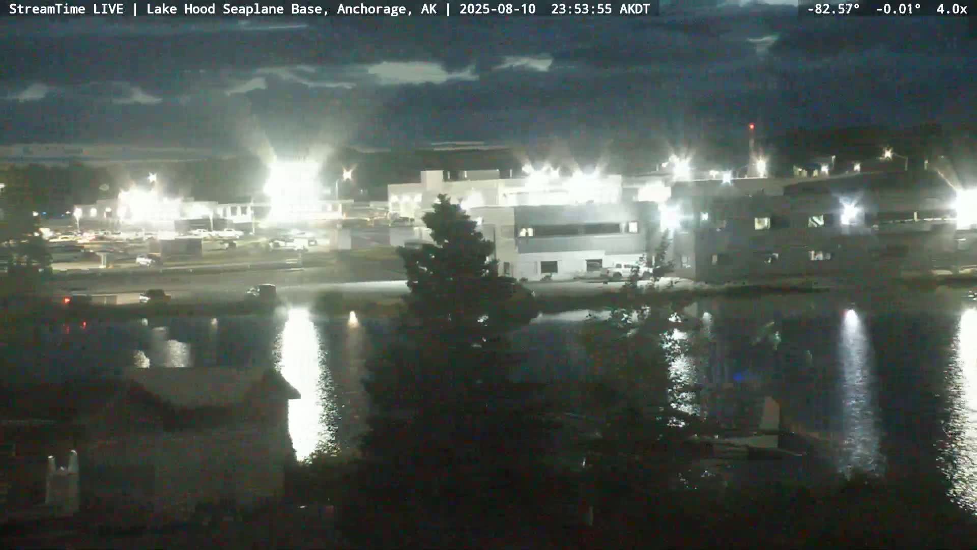 A nighttime view of a building complex beside a calm body of water under a partly cloudy sky.