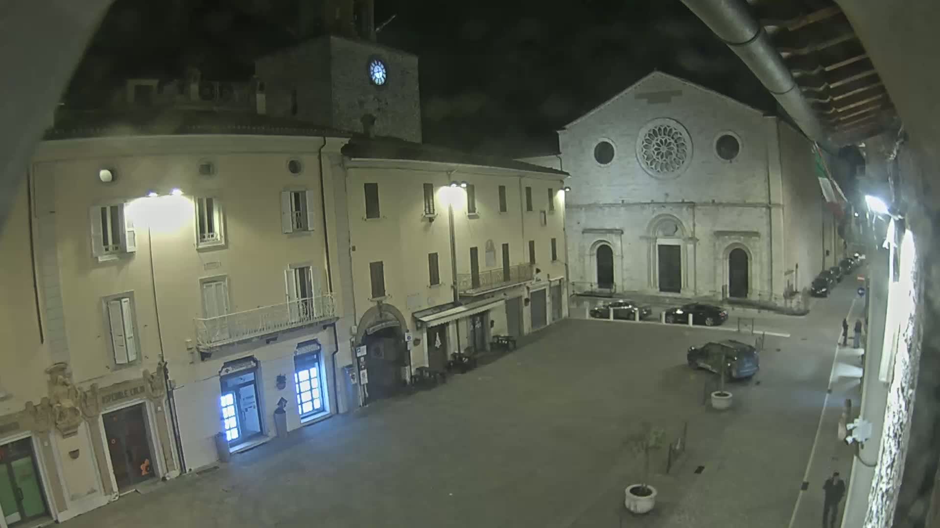 A nighttime view of a town square with several buildings, including a church with a rose window, under a cloudy sky.