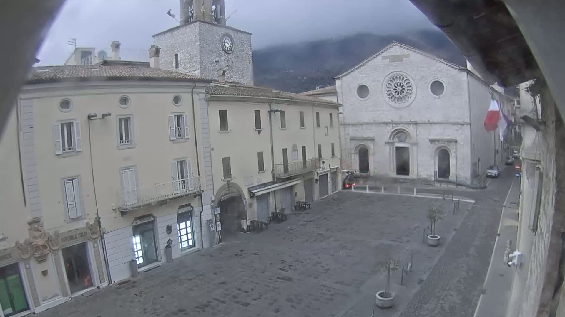 A town square with several buildings, including a church with a rose window, under an overcast sky.