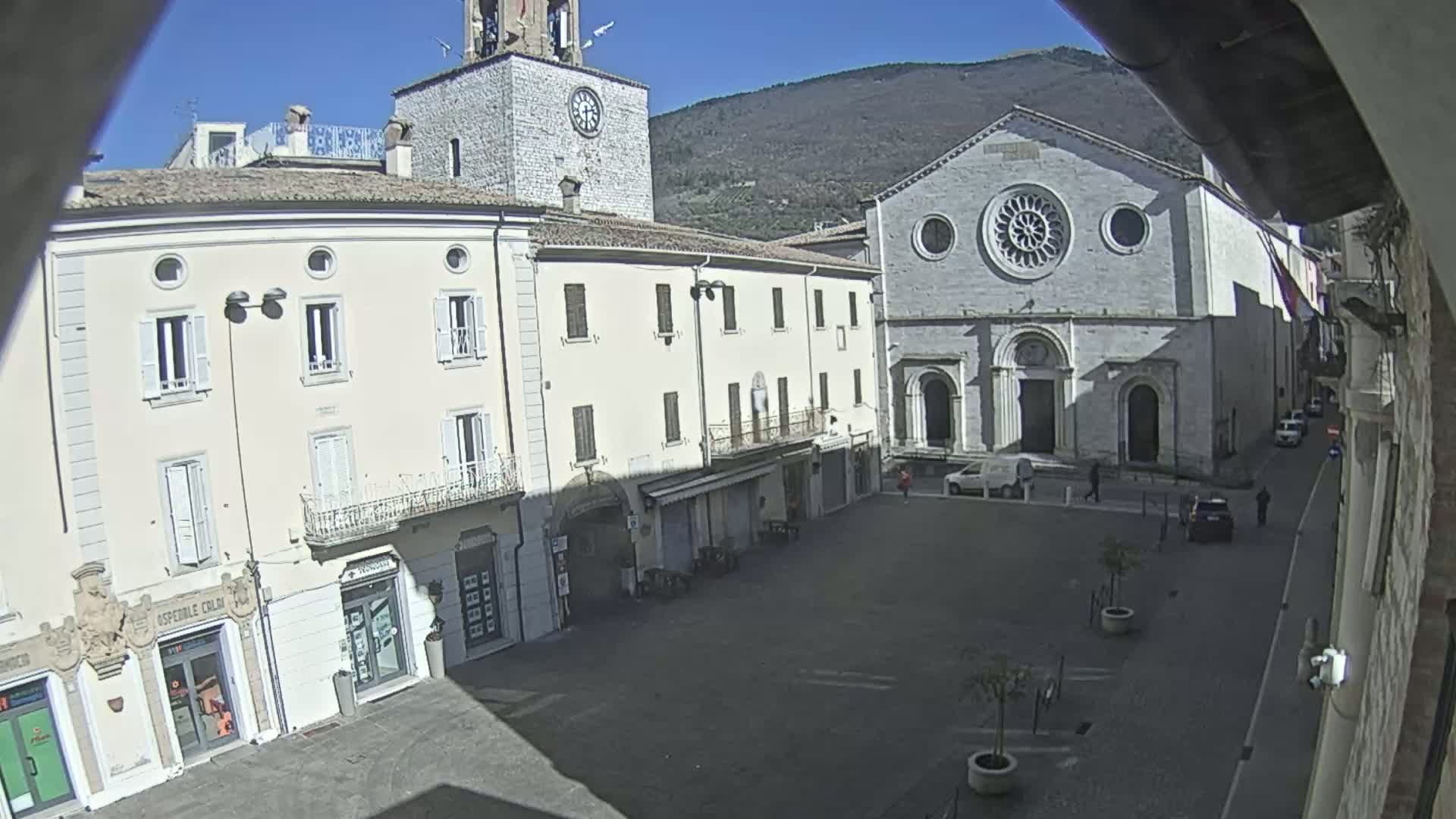 A sunny day reveals a town square with several buildings, including a church with a rose window and a clock tower, surrounded by low buildings.