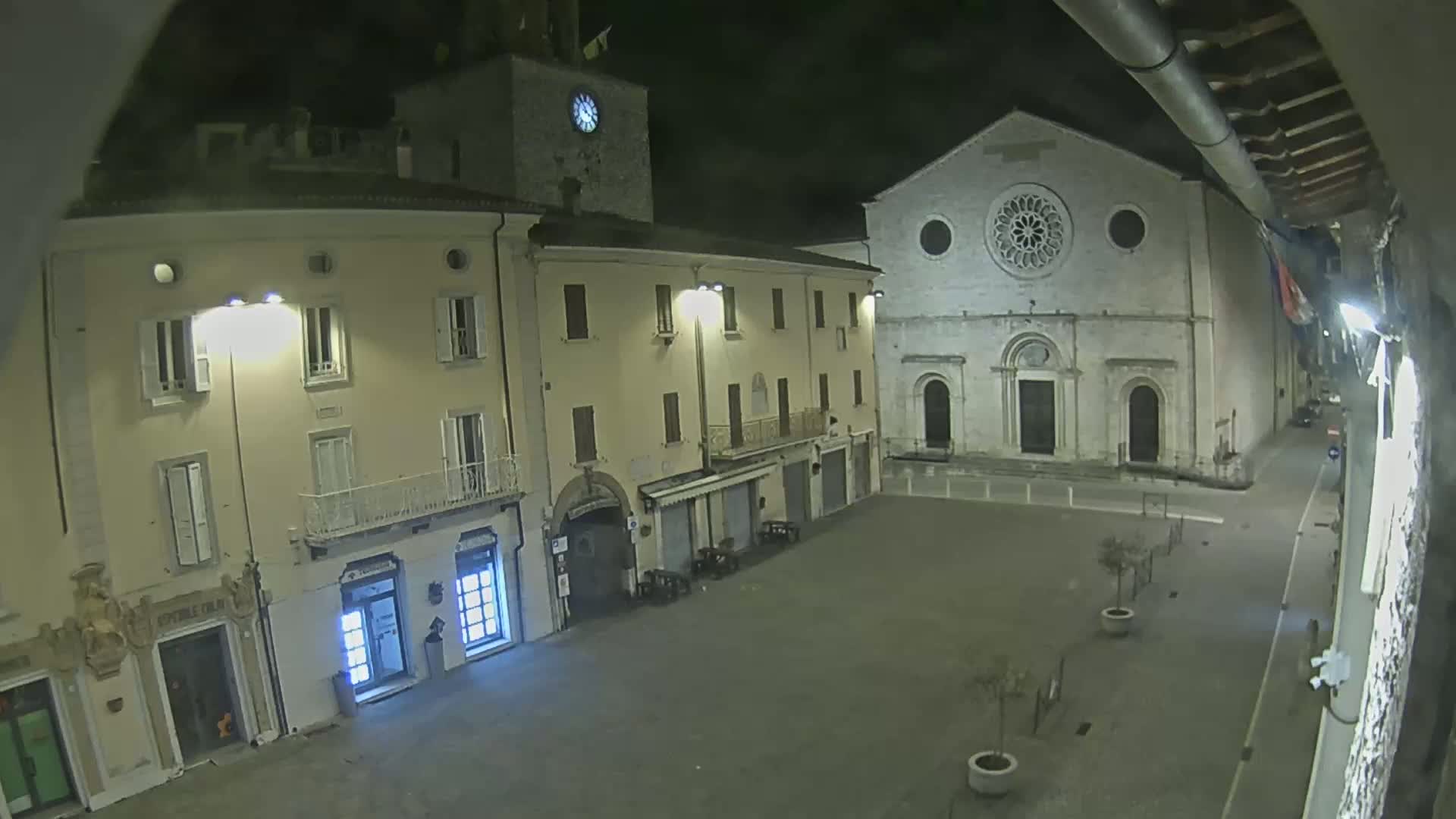 A nighttime view of a town square with buildings, including a church with a rose window, illuminated by streetlights.