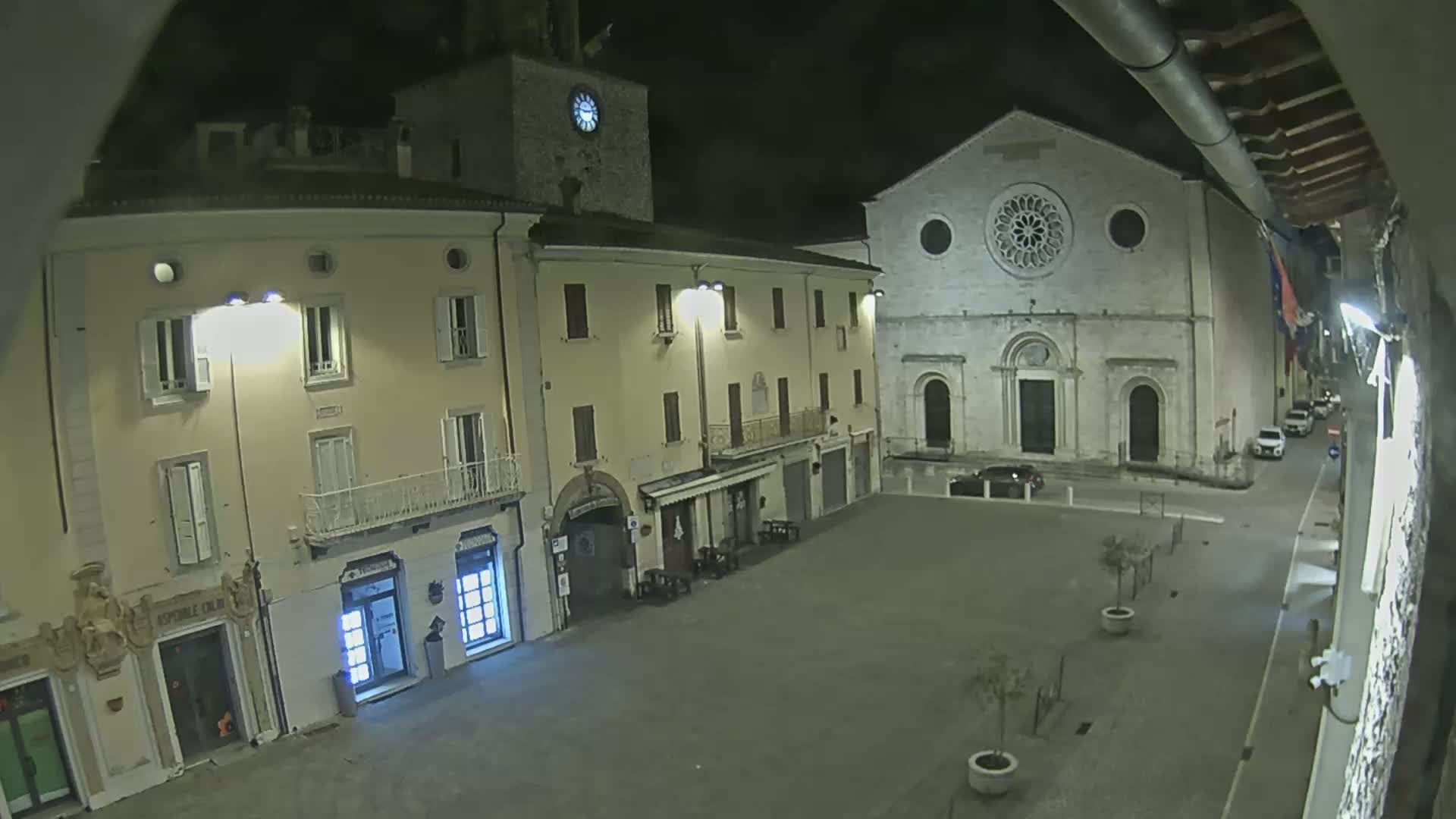 A nighttime view of a town square with buildings, including a church with a rose window, lit by streetlights.