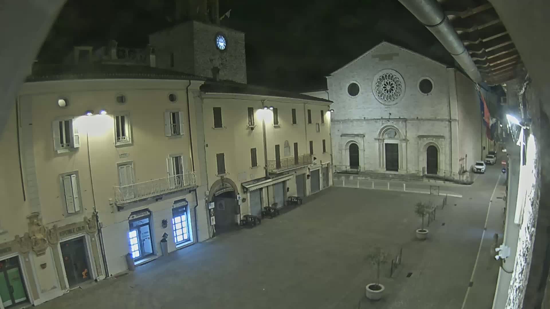 A nighttime view of a town square with several buildings, including a church with a rose window, under dark, clear skies.