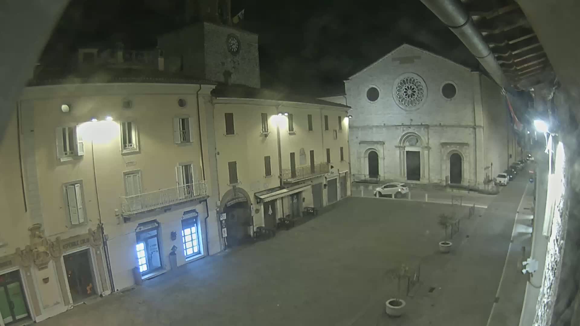 A nighttime view of a town square with buildings, including a church with a rose window, under cloudy skies.