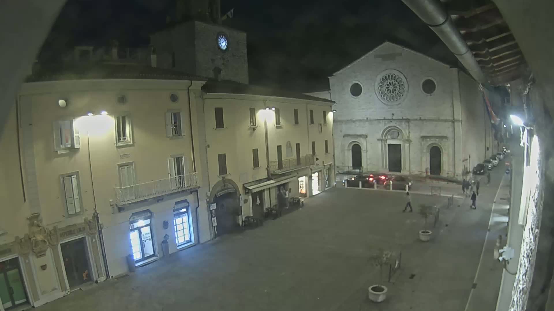 A nighttime view of a town square with several buildings, including a church with a large rose window, under a dark sky.