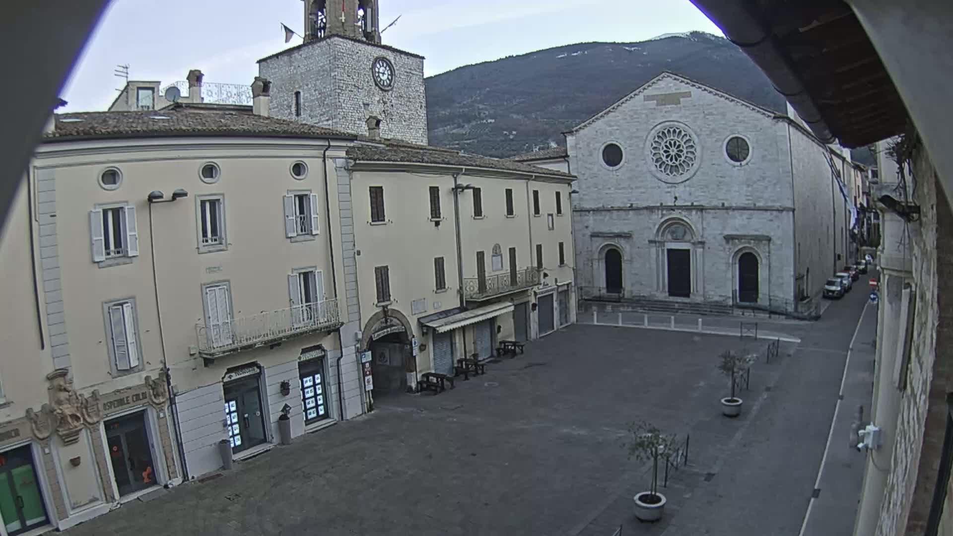 A mostly empty town square is seen on an overcast day, with buildings lining the square, including a large church with a rose window and a clock tower.
