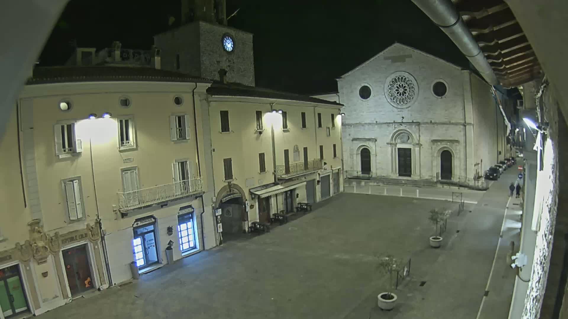 A nighttime view of a town square, featuring several buildings including a church with a large rose window, illuminated by streetlights under a clear sky.