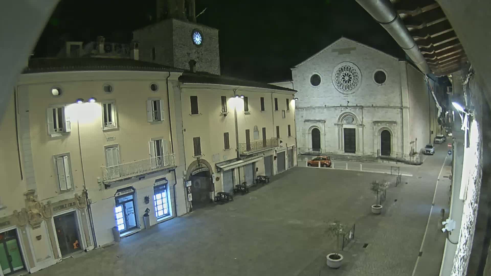 A nighttime view of a town square with buildings, including a church with a rose window, and a clock tower.