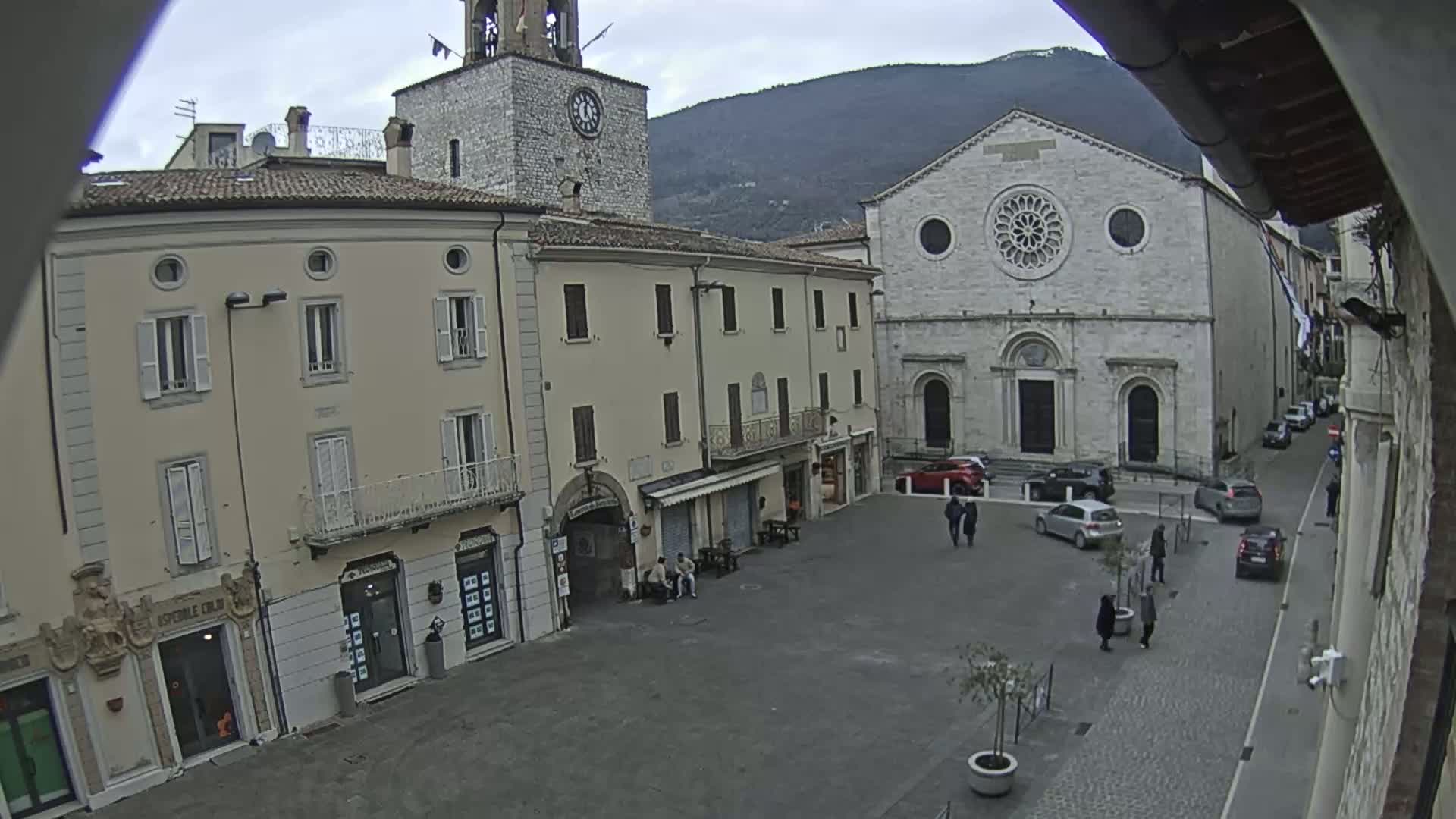 A town square with several buildings, including a clock tower and a large church, is seen on an overcast day.