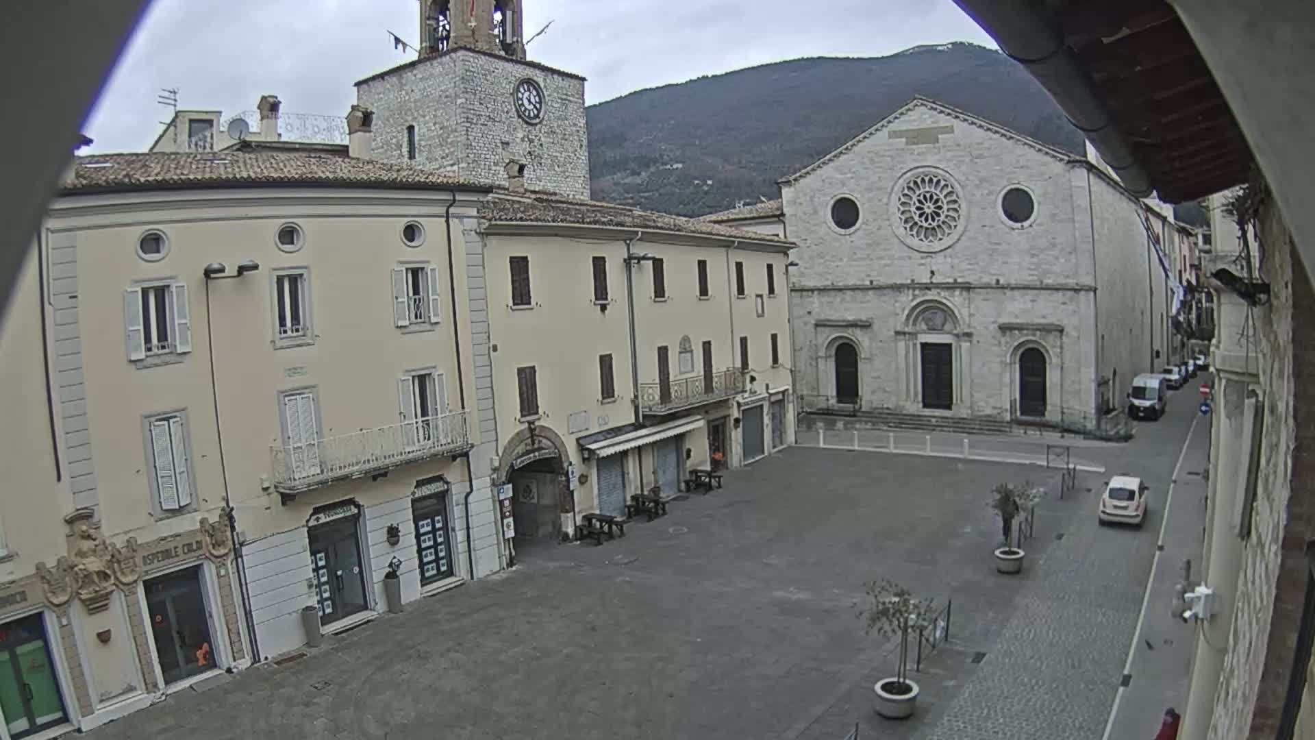 A town square, under an overcast sky, is surrounded by buildings including a clock tower and a large stone church.
