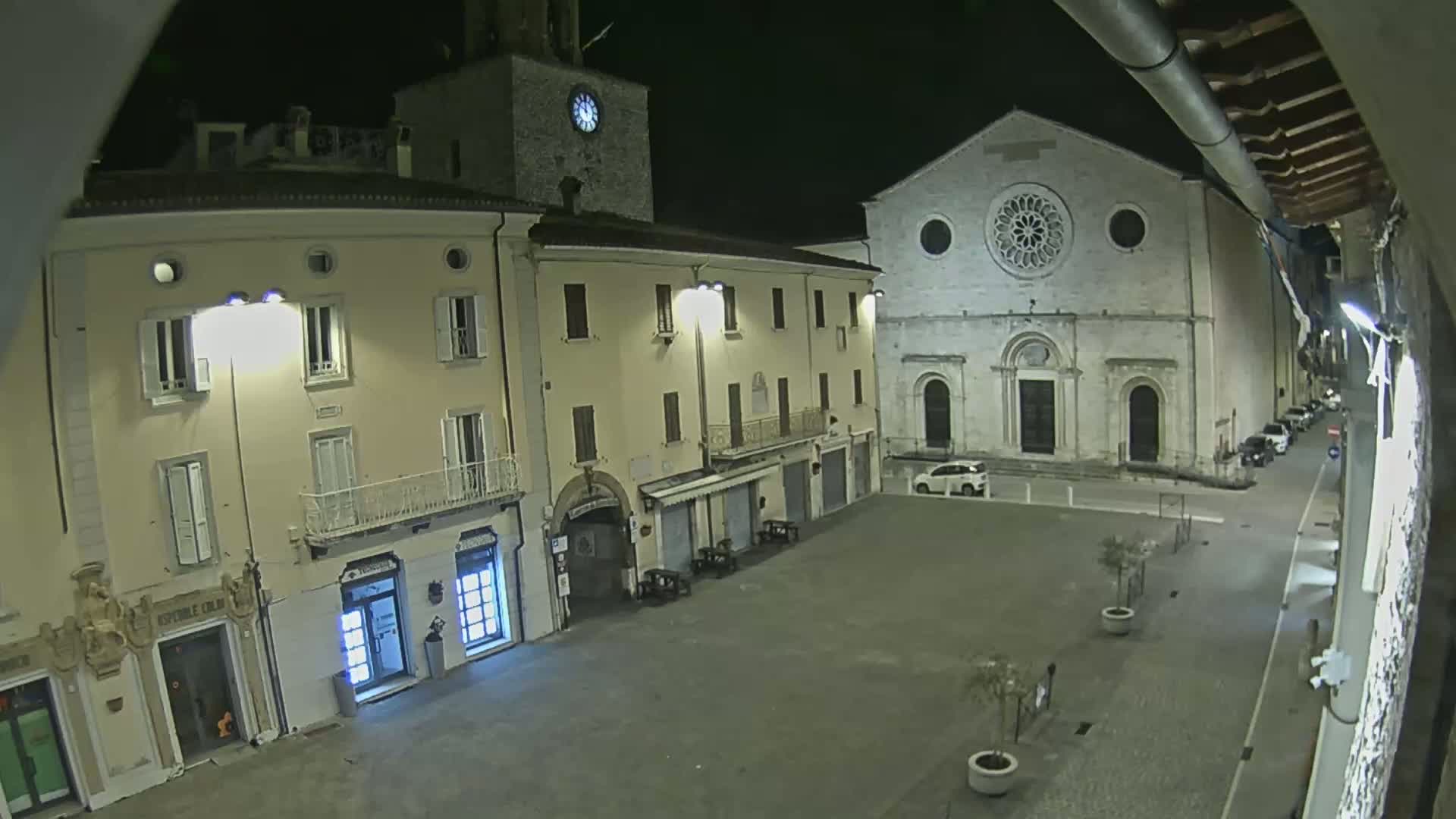 A nighttime view of a town square shows several buildings, including a church with a rose window, under clear, dark skies.