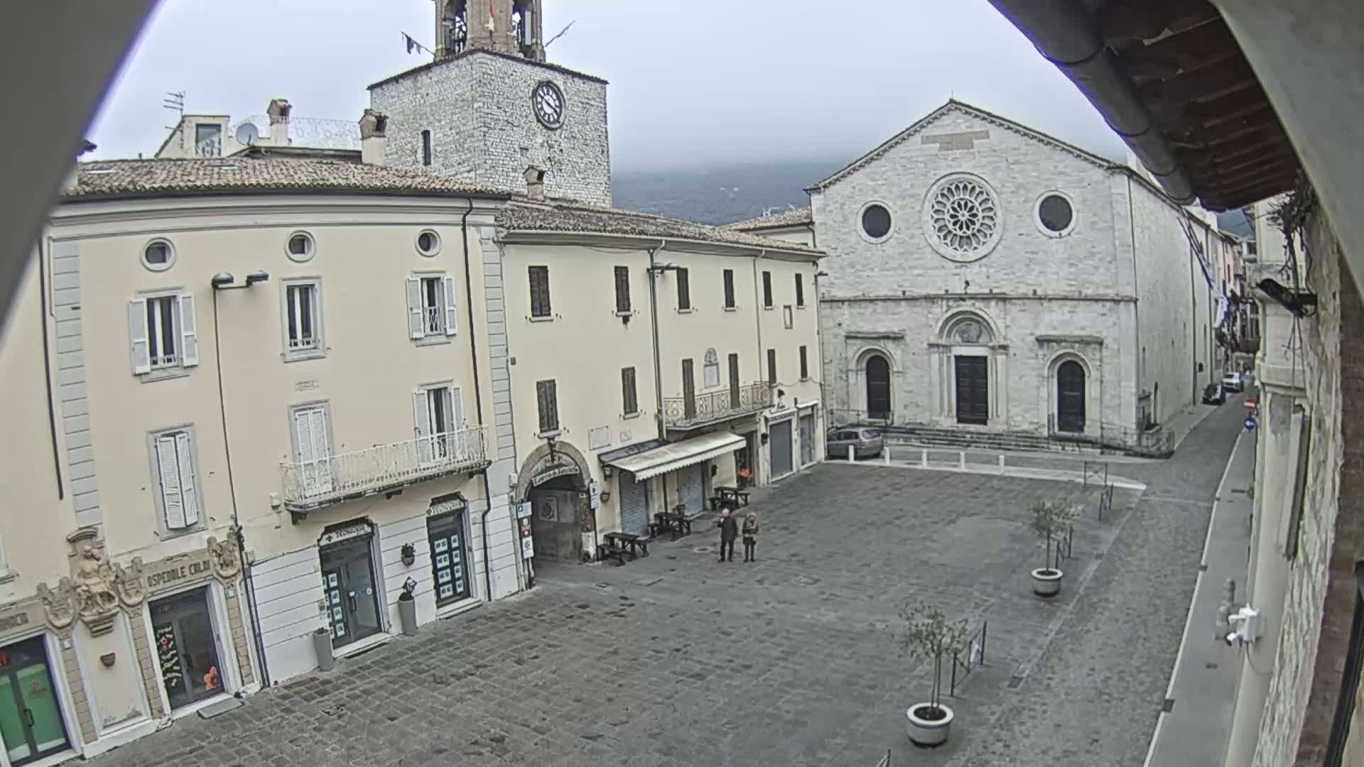 A town square with several stone buildings, including a church with a rose window, under an overcast sky.