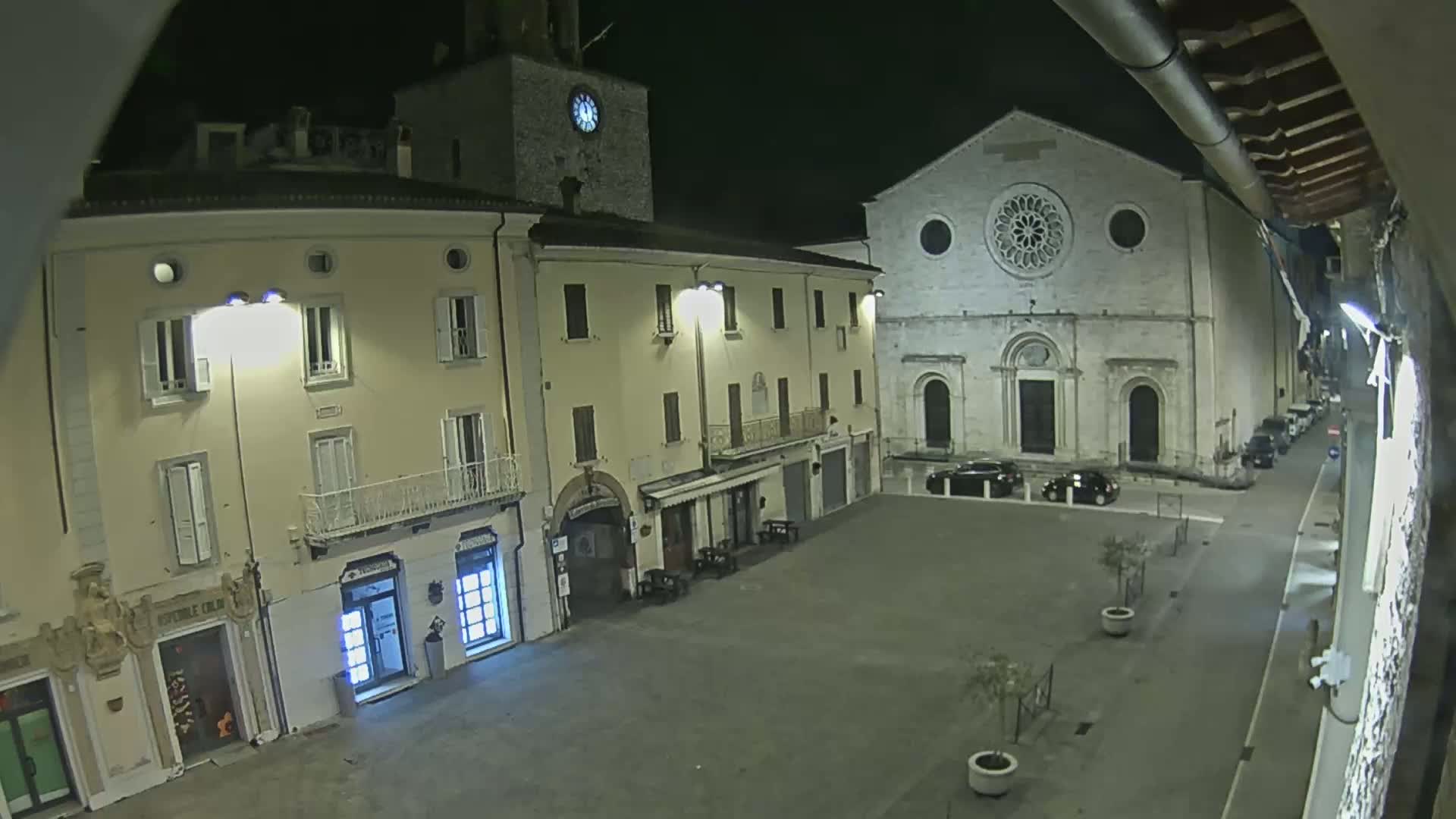 A nighttime view of a town square with several buildings, including a church with a rose window, illuminated by streetlights.