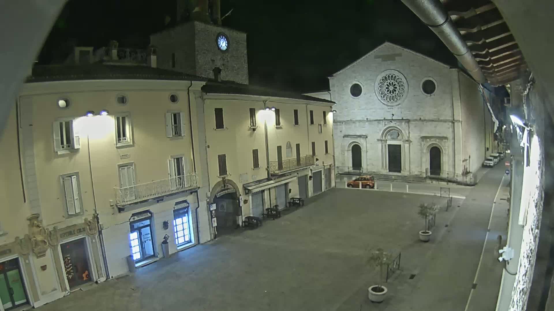 A nighttime view of a town square with several buildings, including a church with a large rose window, illuminated by streetlights.