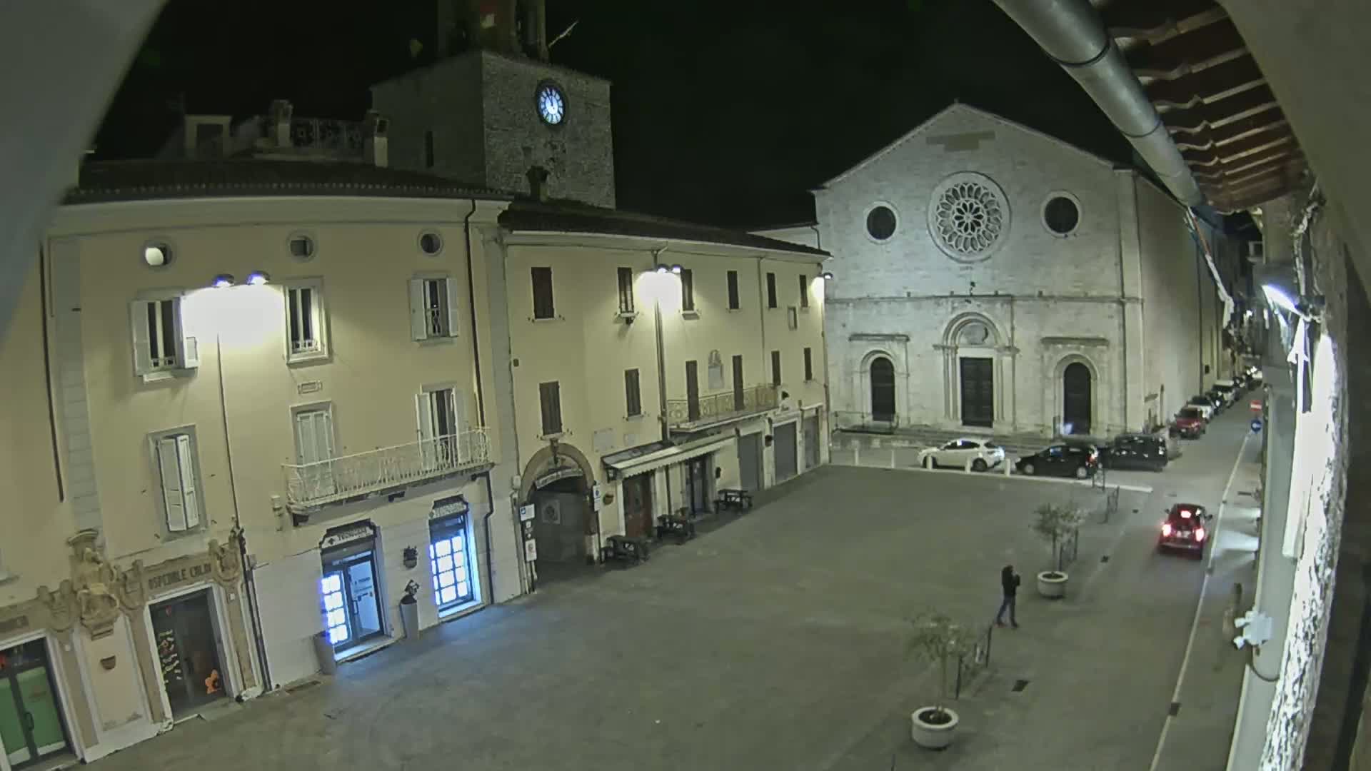A nighttime view of a town square with several buildings, including a church with a large rose window, illuminated by streetlights.